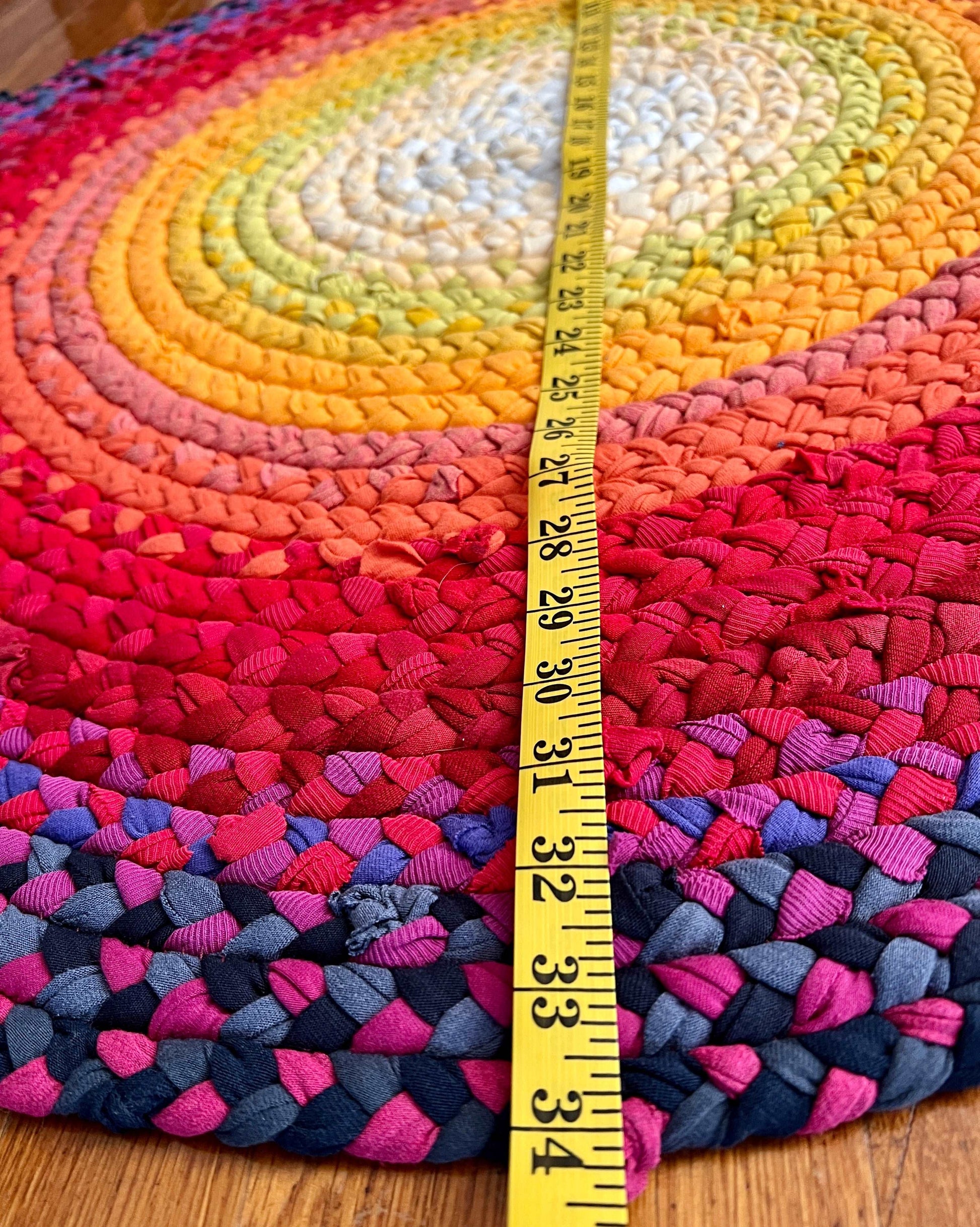 side view of the sunset ombré braided rug. a measuring tape across the rug, closeup of 24 inches, which is the diameter of the rug.