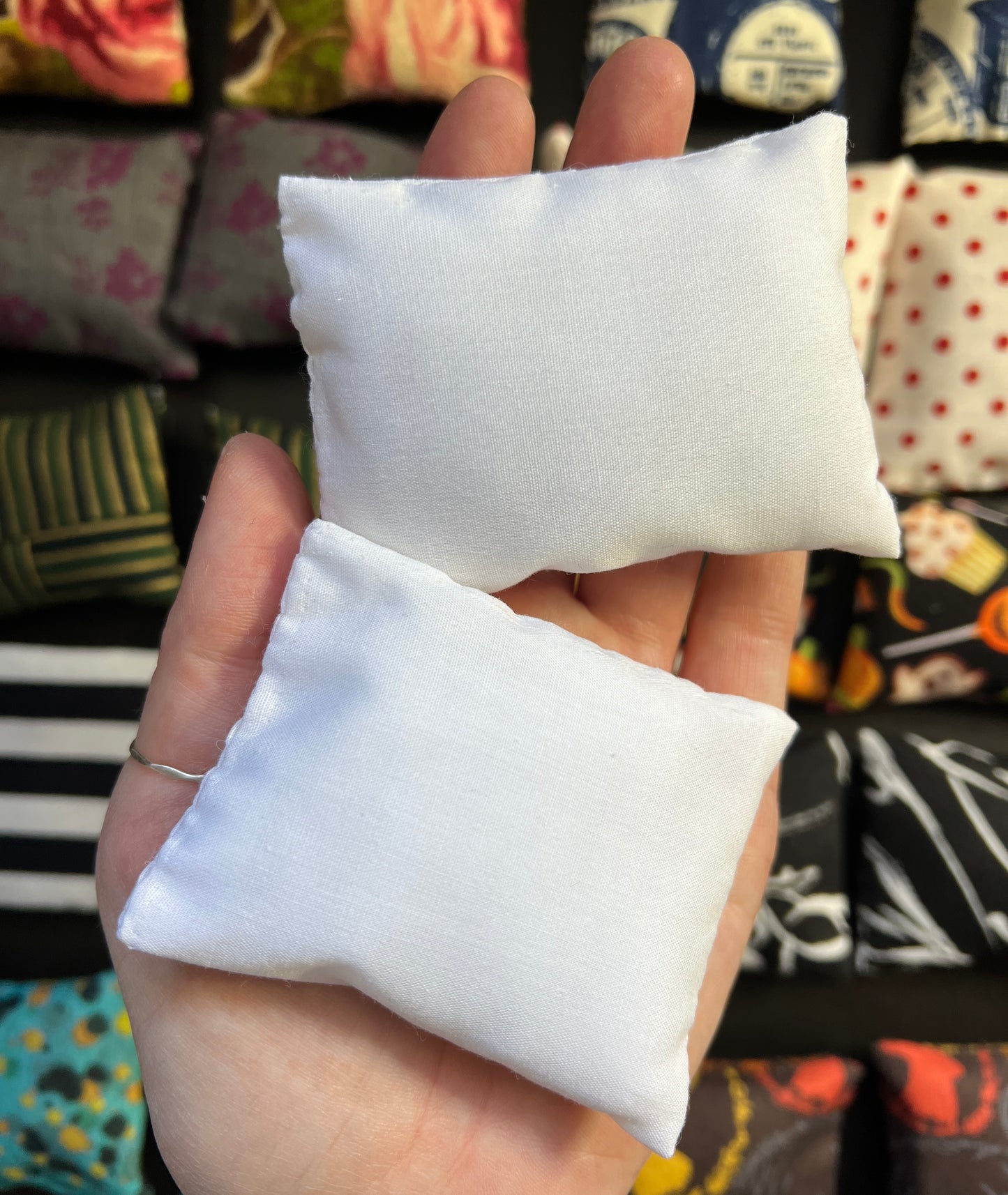a hand holds a pair of Barbie pillows, for scale. solid white. other pillows in distance