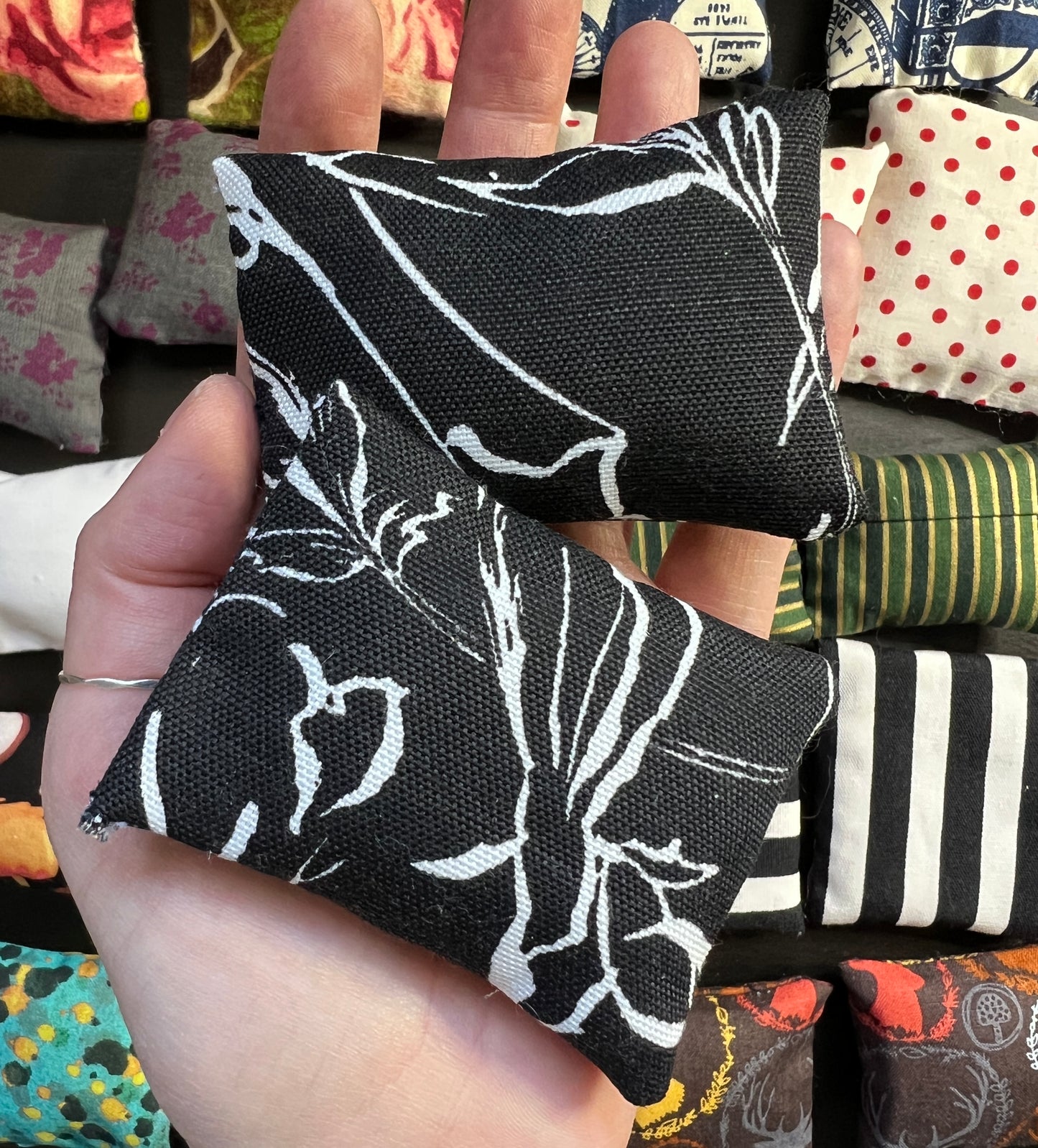 a hand holds a pair of Barbie pillows, for scale. white floral lines on a black background. other pillows in distance