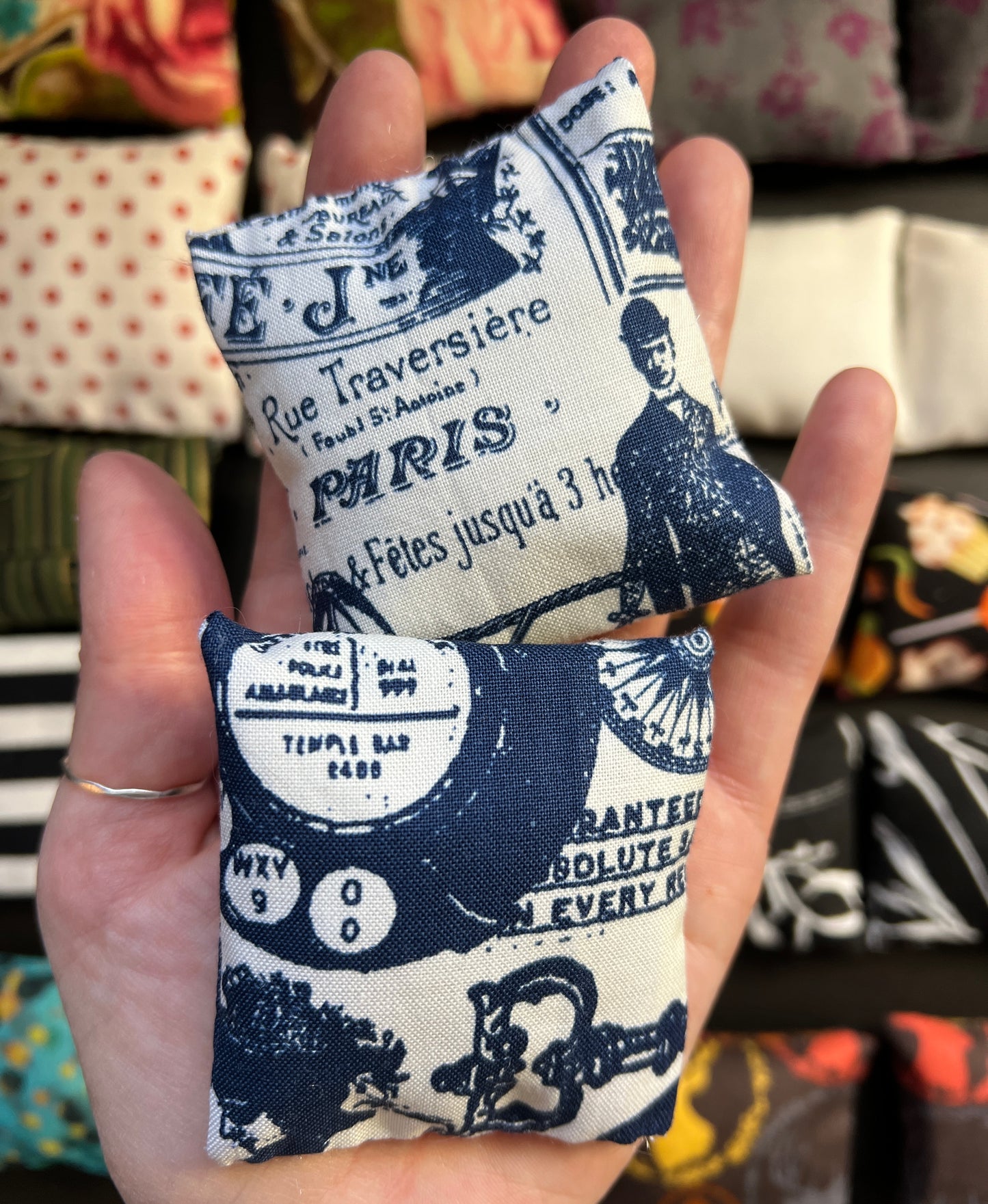 a hand holds a pair of Barbie pillows, for scale. navy blue nostalgia graphics on an ivory background. other pillows in distance