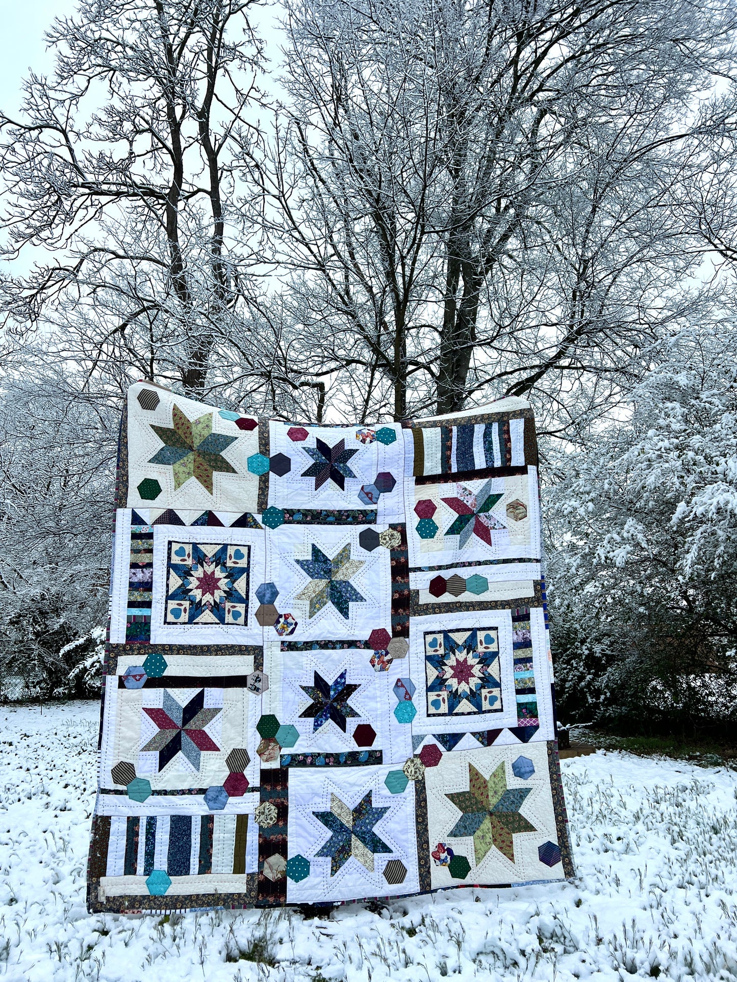 A quilt with eight point stars and quilted hexies, in a snowy scene