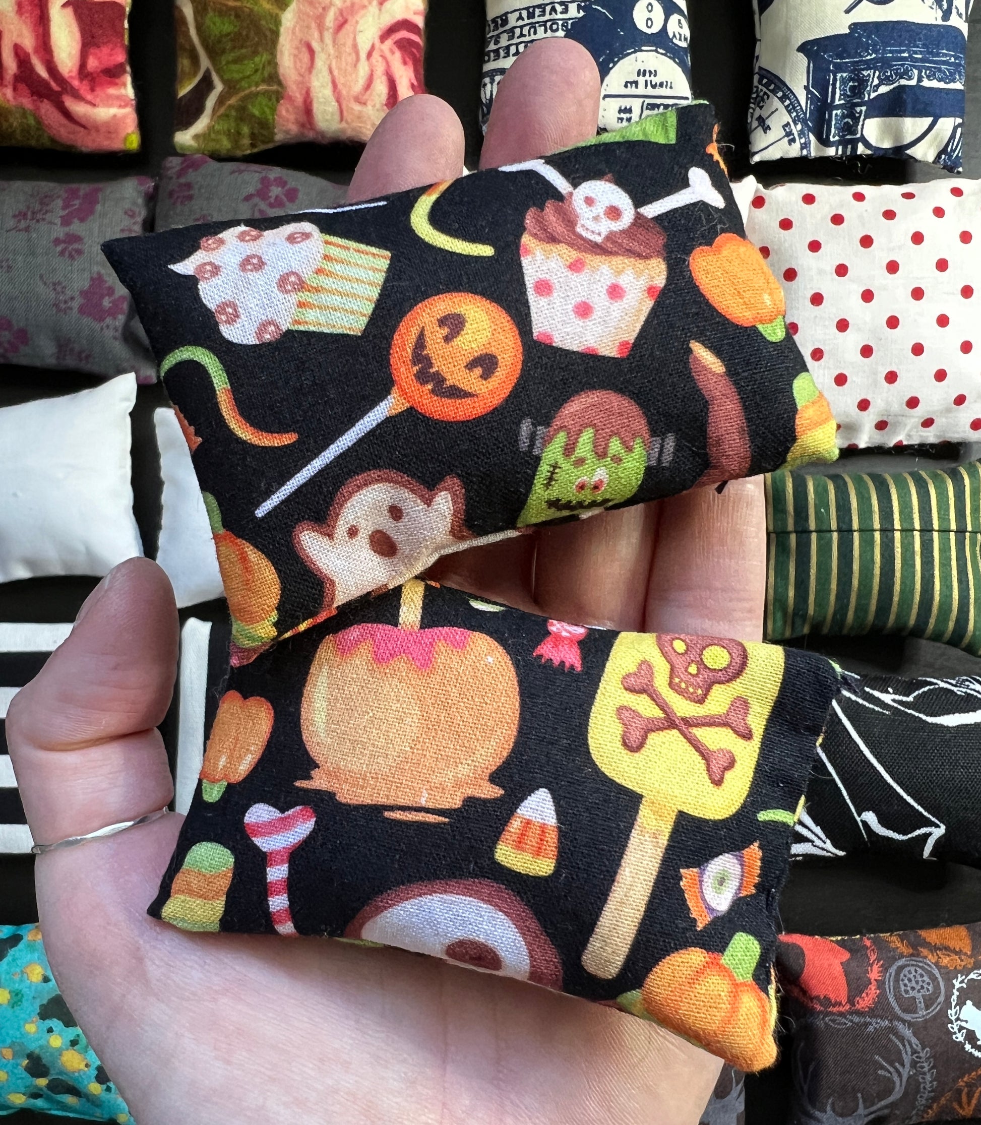 a hand holds a pair of Barbie pillows, for scale. various halloween candy graphics on a black background. other pillows in distance