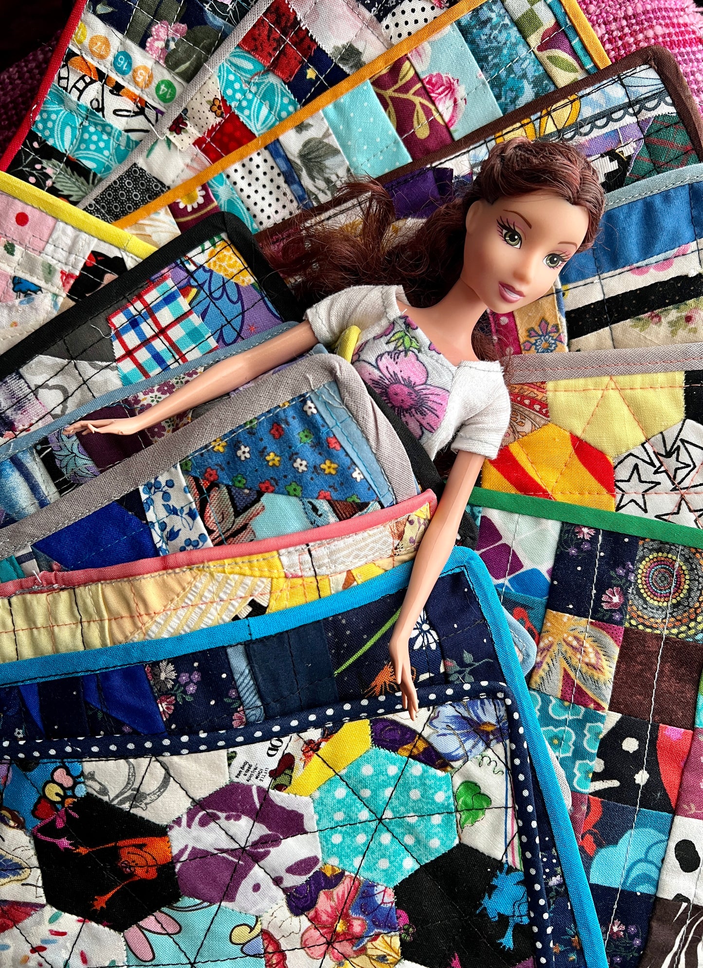 Barbie doll laying on and under an array of colorful quilts, looking very comfy