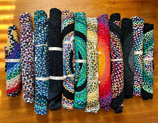 An assortment of colorful vibrant and unique tshirt rugs, all rolled up neatly and laid next to each other, aerial view on a wood floor