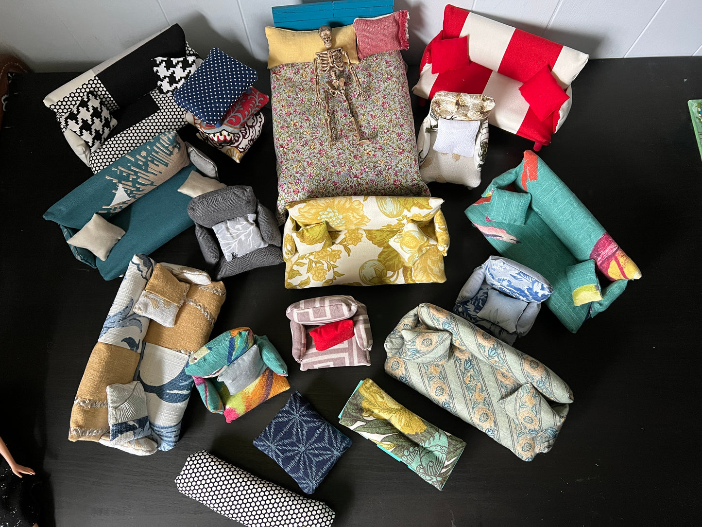 Big group of small furniture pieces, chairs, couches, and ottomans, benches, and a bed with mattress. A miniature skeleton guy is on the bed for scale