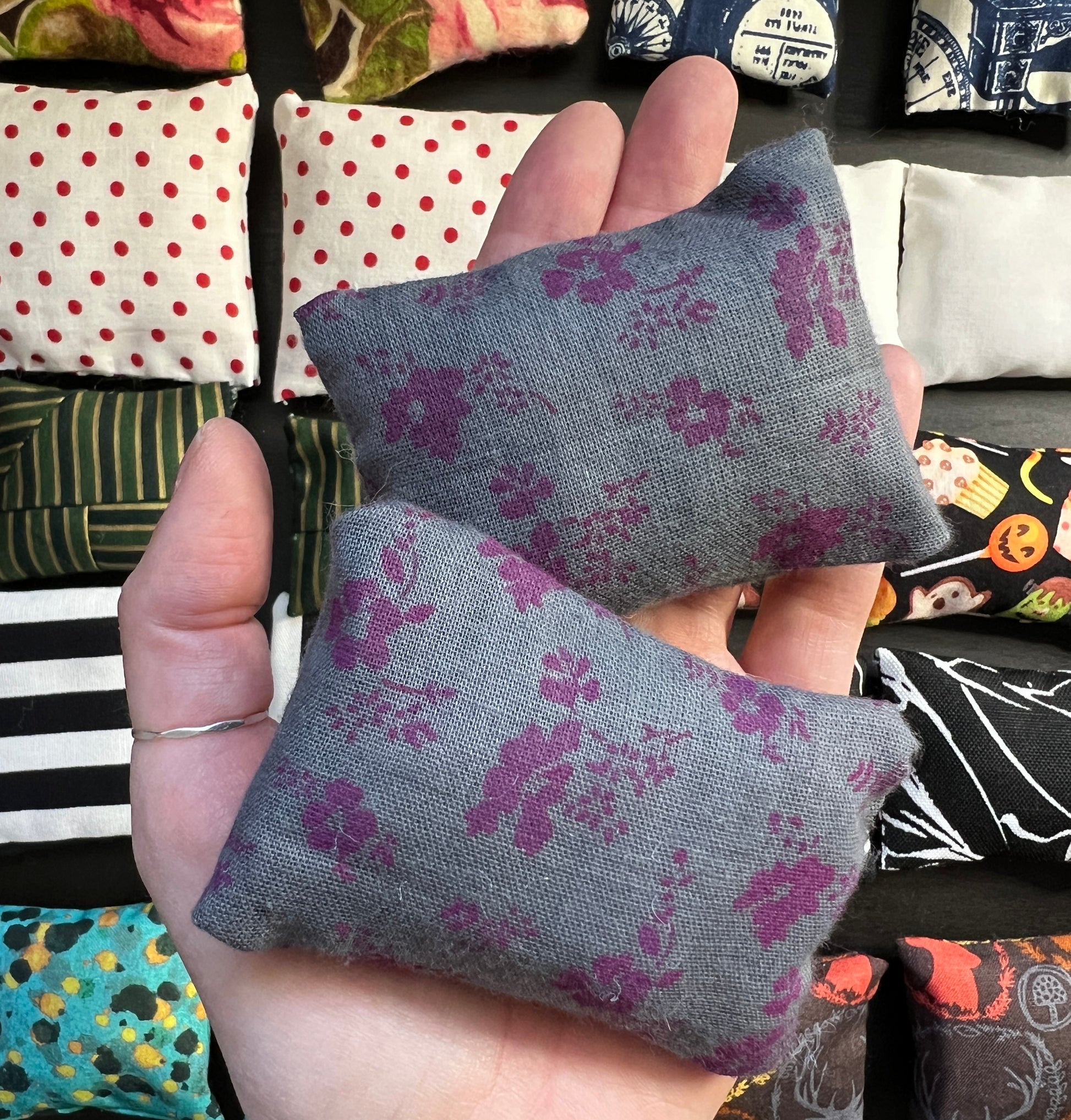 a hand holds a pair of Barbie pillows, for scale. little purple flowers on a grey background. other pillows in distance