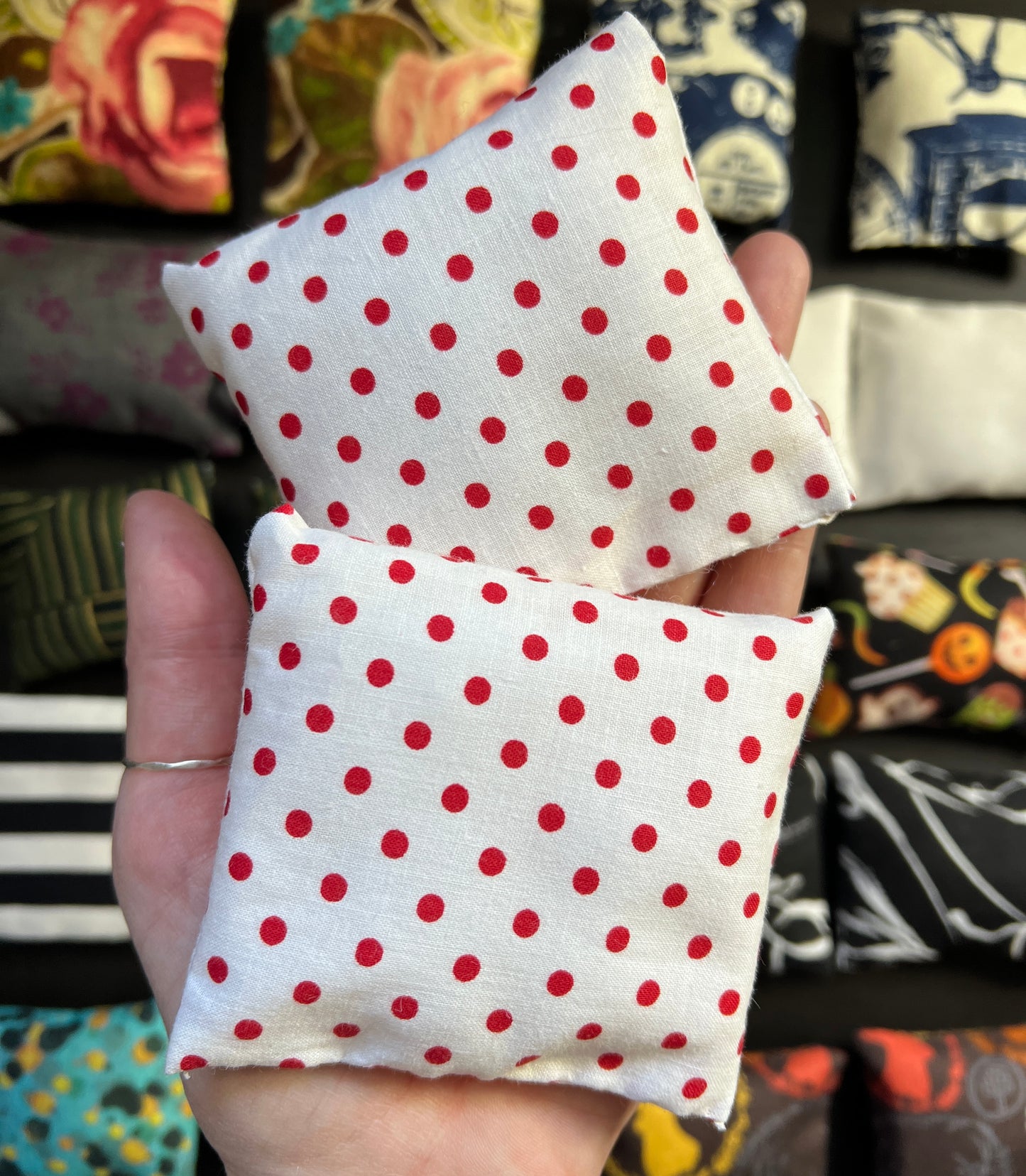a hand holds a pair of Barbie pillows, for scale. red polkadots on a white background. other pillows in distance