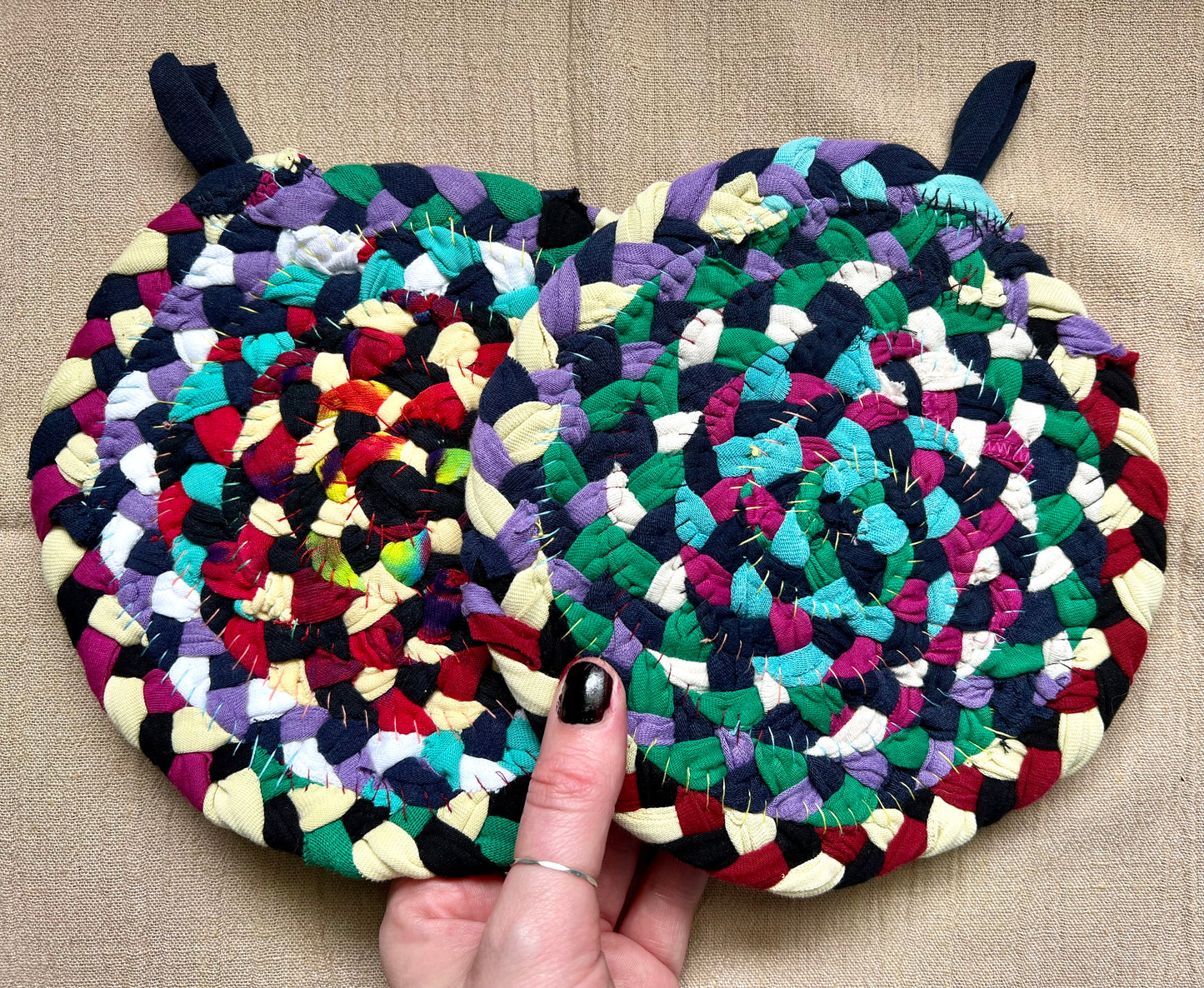 The back of two trivet potholders, to show off stitching, held against a linen surface.