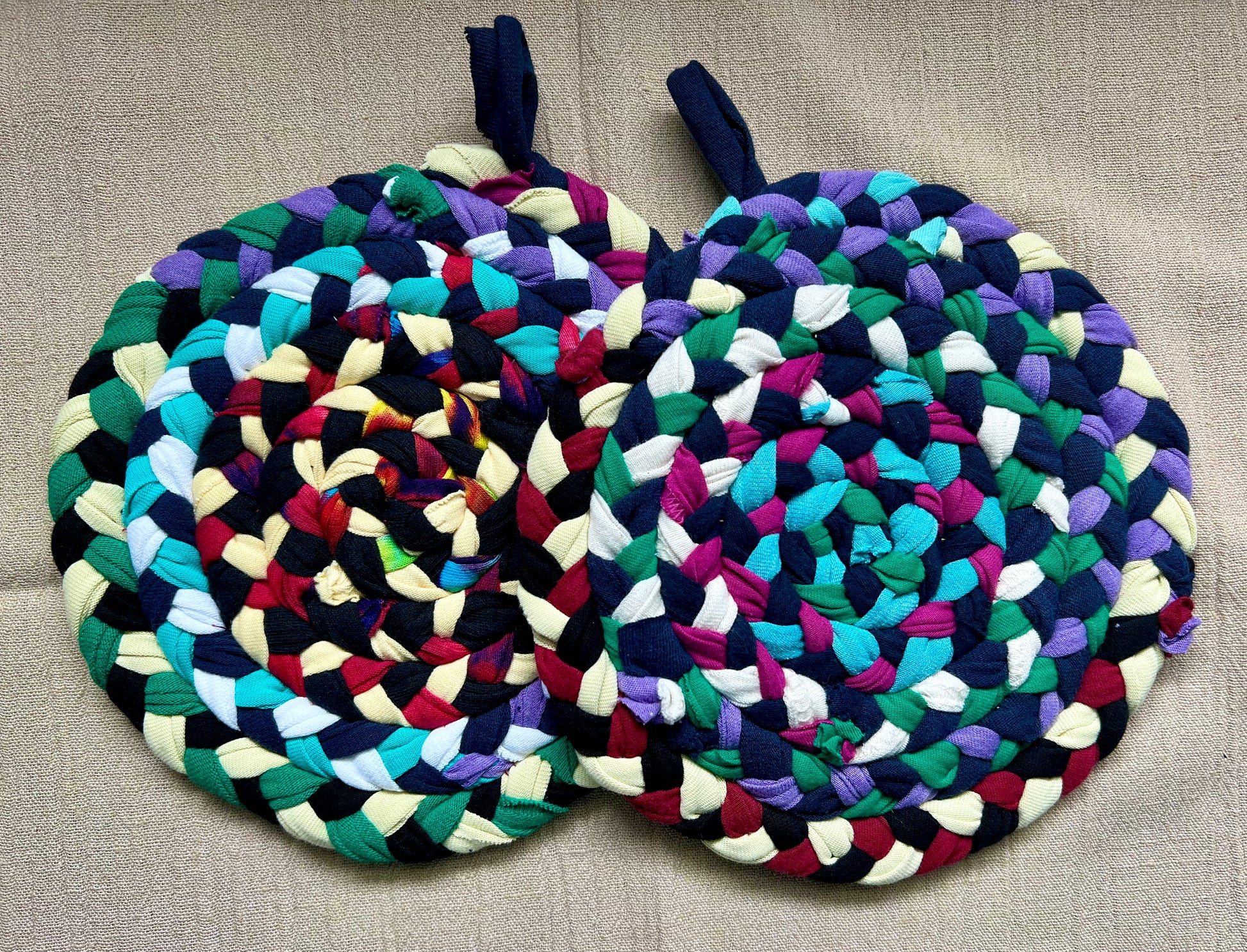 A set of two trivet potholders, side by side, lay flat on a linen surface.