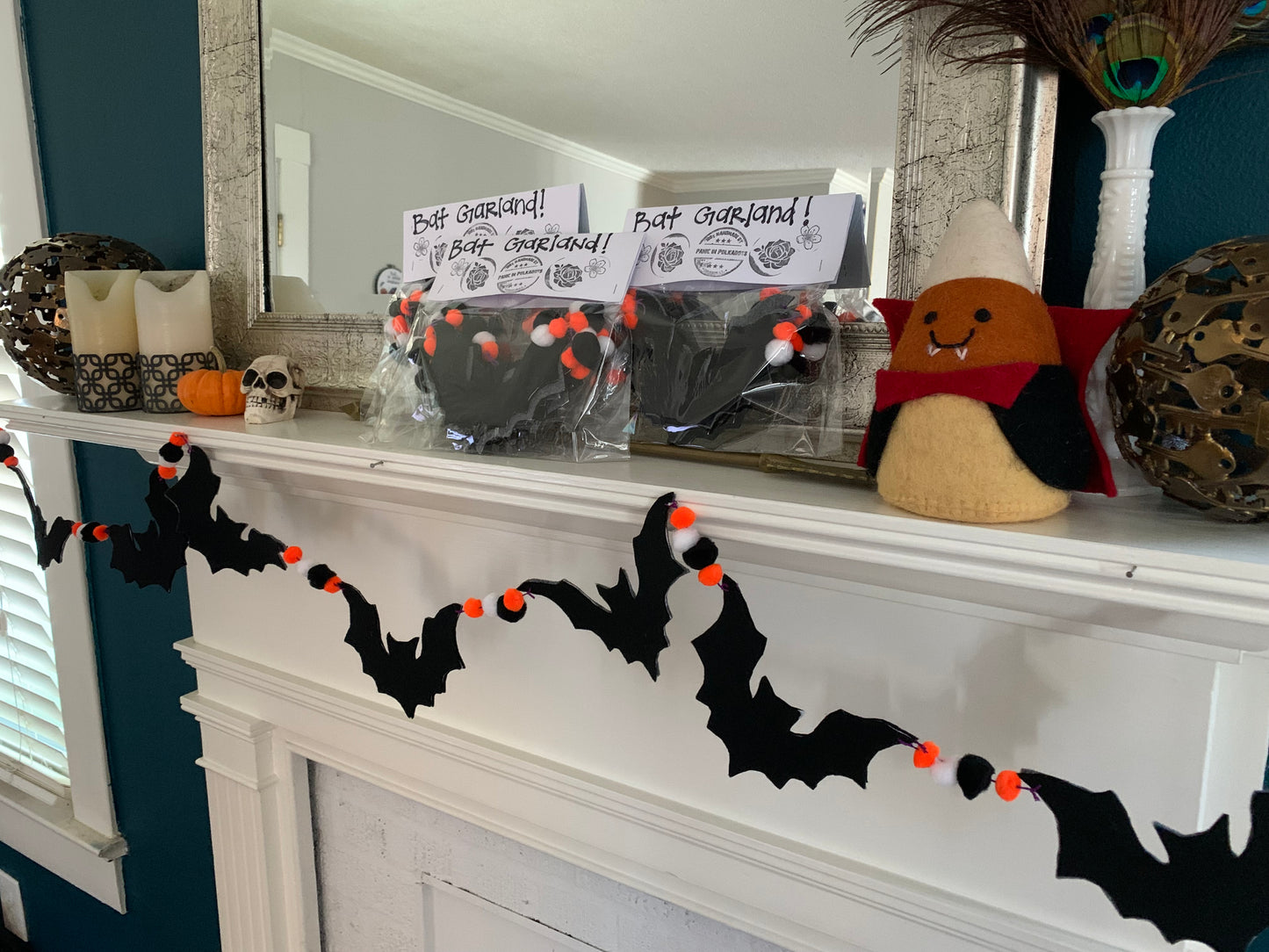 closeup of bat garland on display, and packaged bat garlands on top of mantle. Other halloween decorations surround them