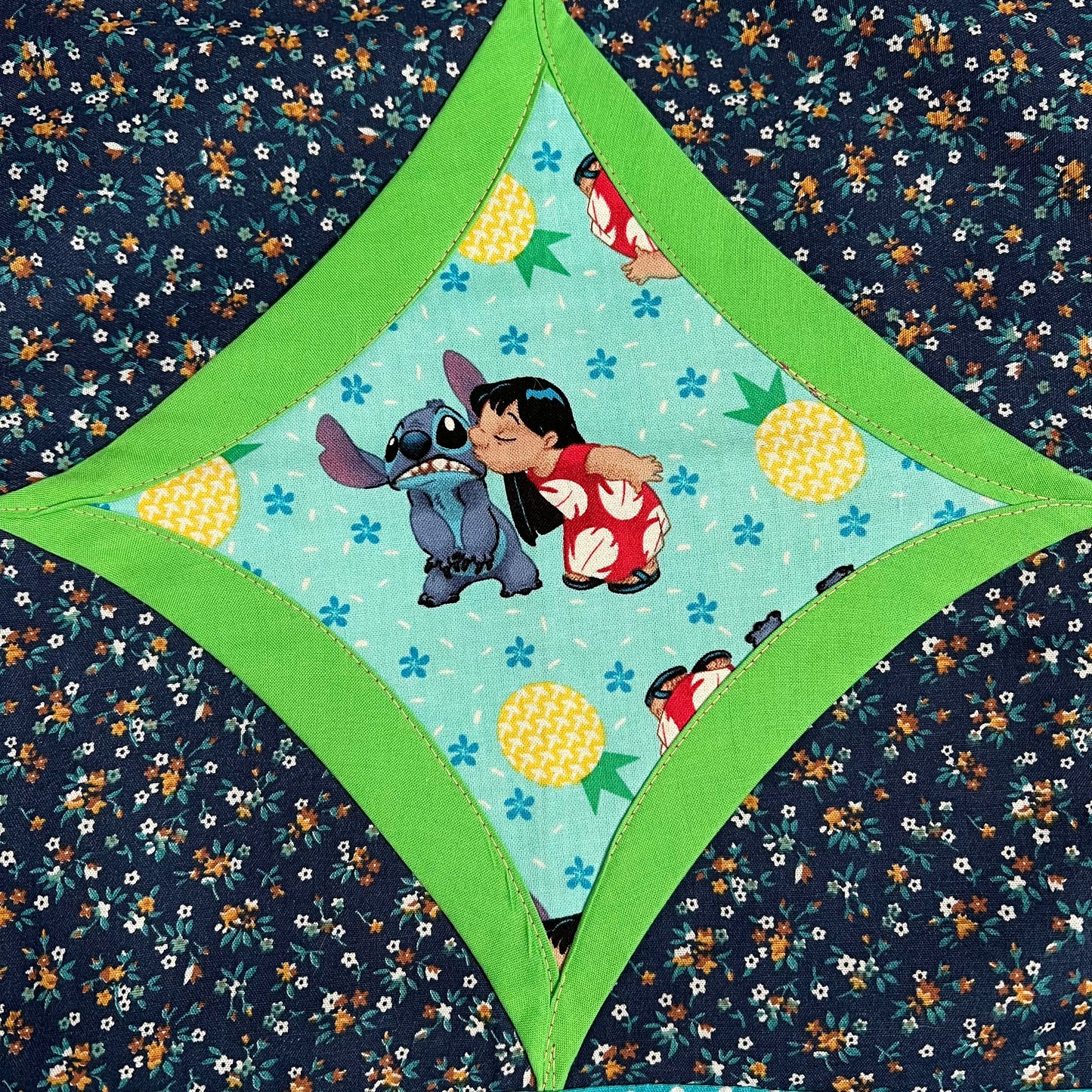 Lilo and Stitch fabric square, surrounded by neon green and then dark navy floral fabrics