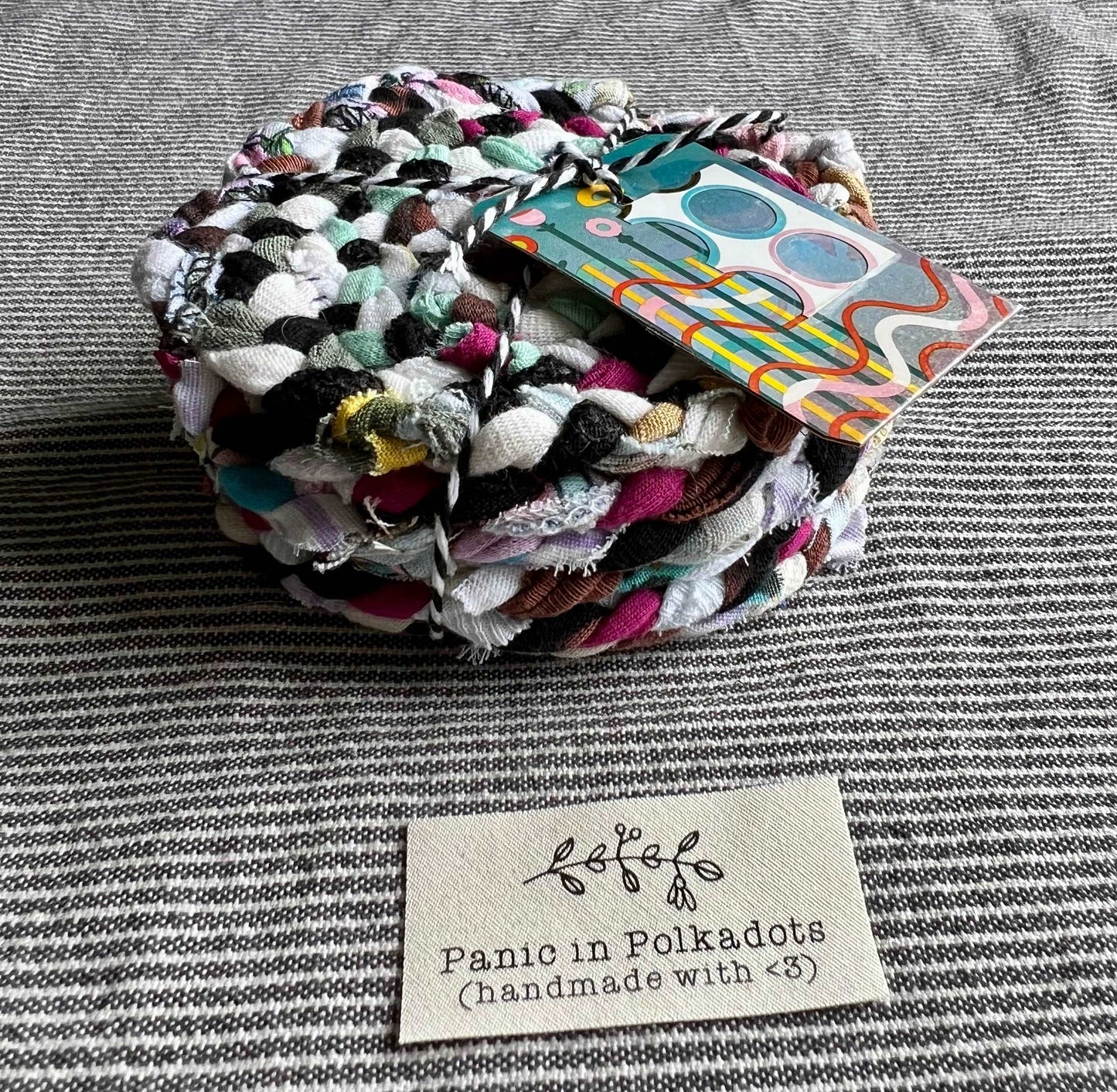 A set of six coasters, bound by string in a stack, with a Panic in Polkadots label in front
