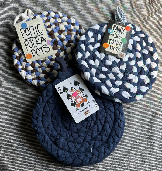 Three sets of trivet potholders, all laid together in a pile. Each set has a playing card with info about Panic in Polkadots.