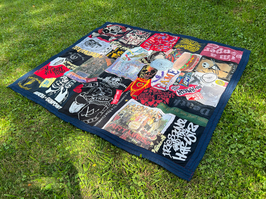 Side view at an angle, of a tee shirt quilt, with bright colors, mostly red, and a navy blue border