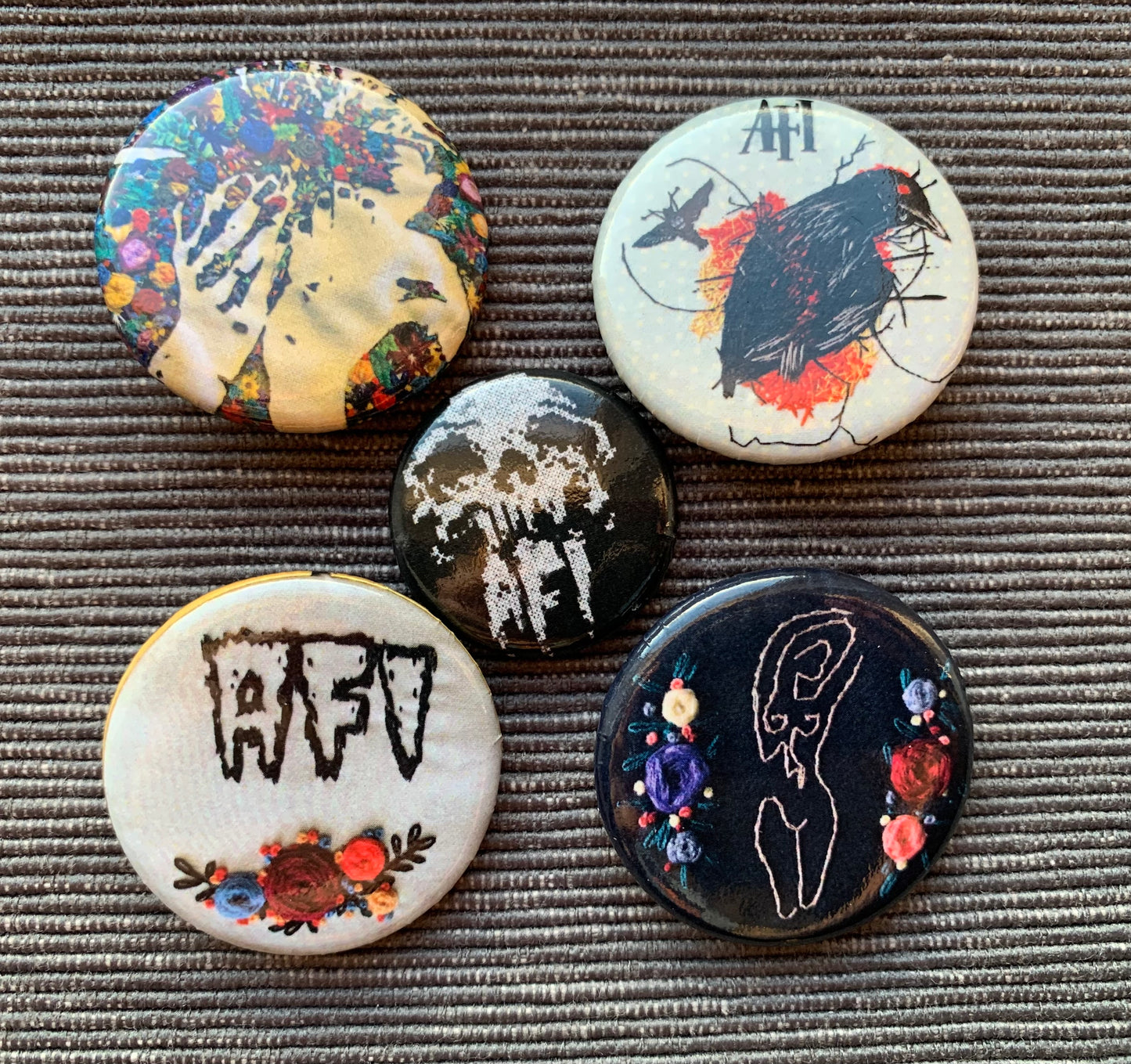 A group of five pinback buttons, against a textured grey background