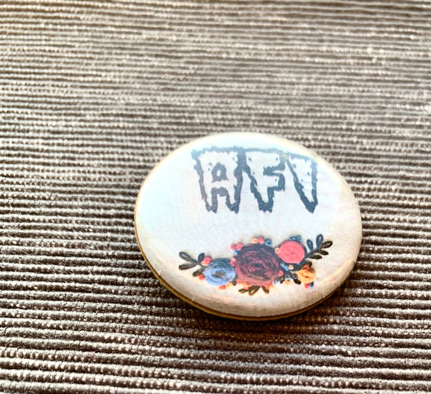 AFI flowers pinback button, closeup, against a grey textured background.