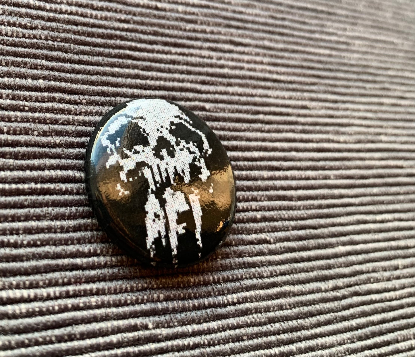 AFI skull pinback button, closeup, against a grey textured background.