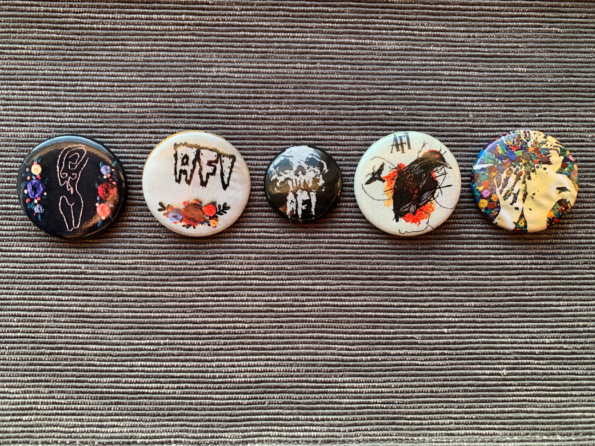 A set of pinback buttons, lined up in a horizontal row, against a grey textured background.