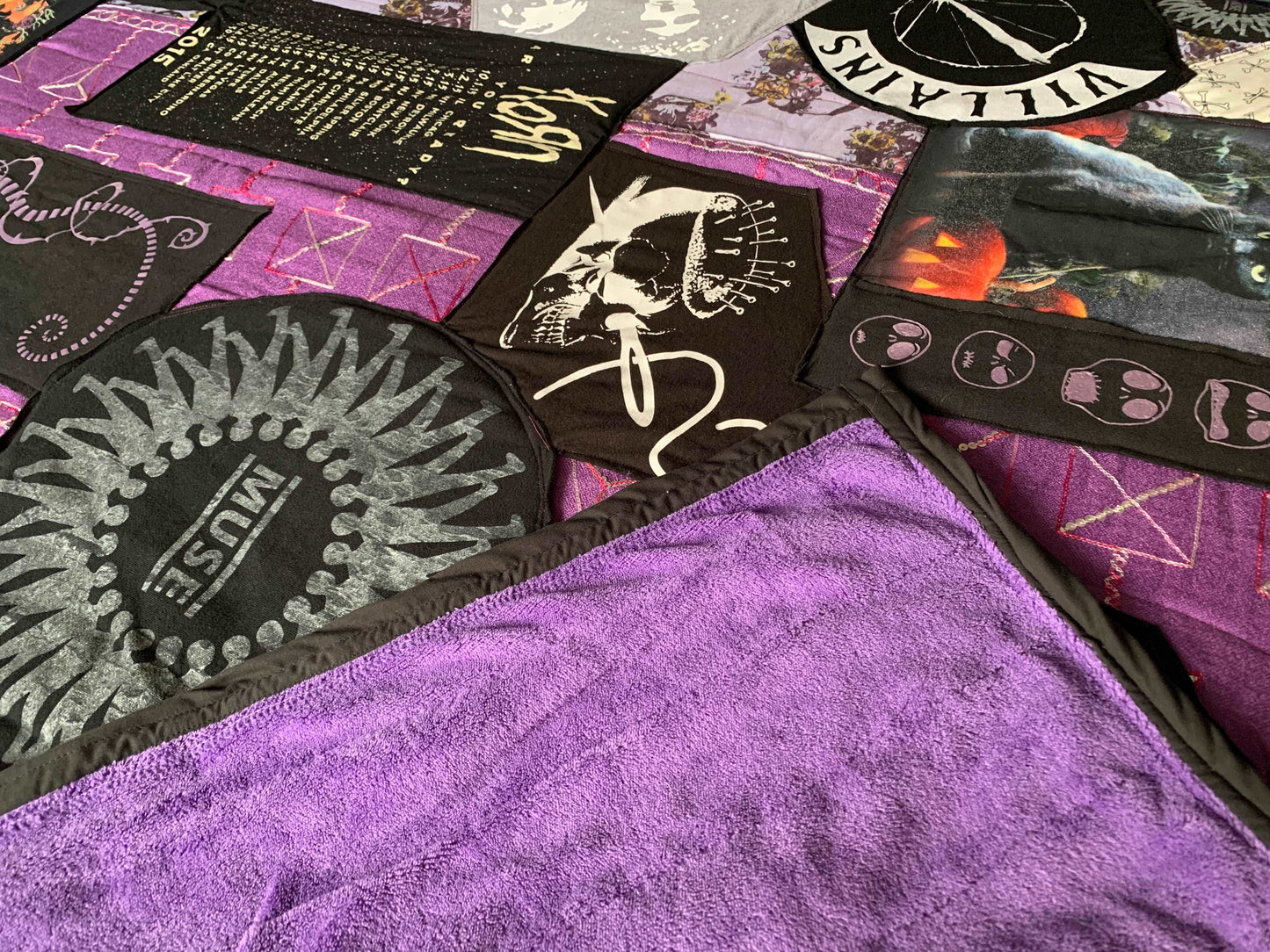 A purple and black tshirt quilt, with a corner folded over to show off the plush fuzzy backing in purple.
