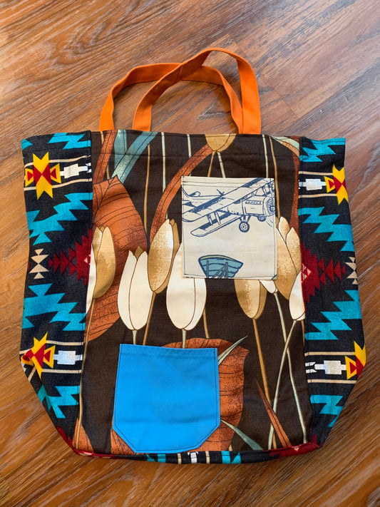 A tote bag, created out of scrappy canvas pieces of large tulip print, and southwestern print sides, with an apron strap set of handles.