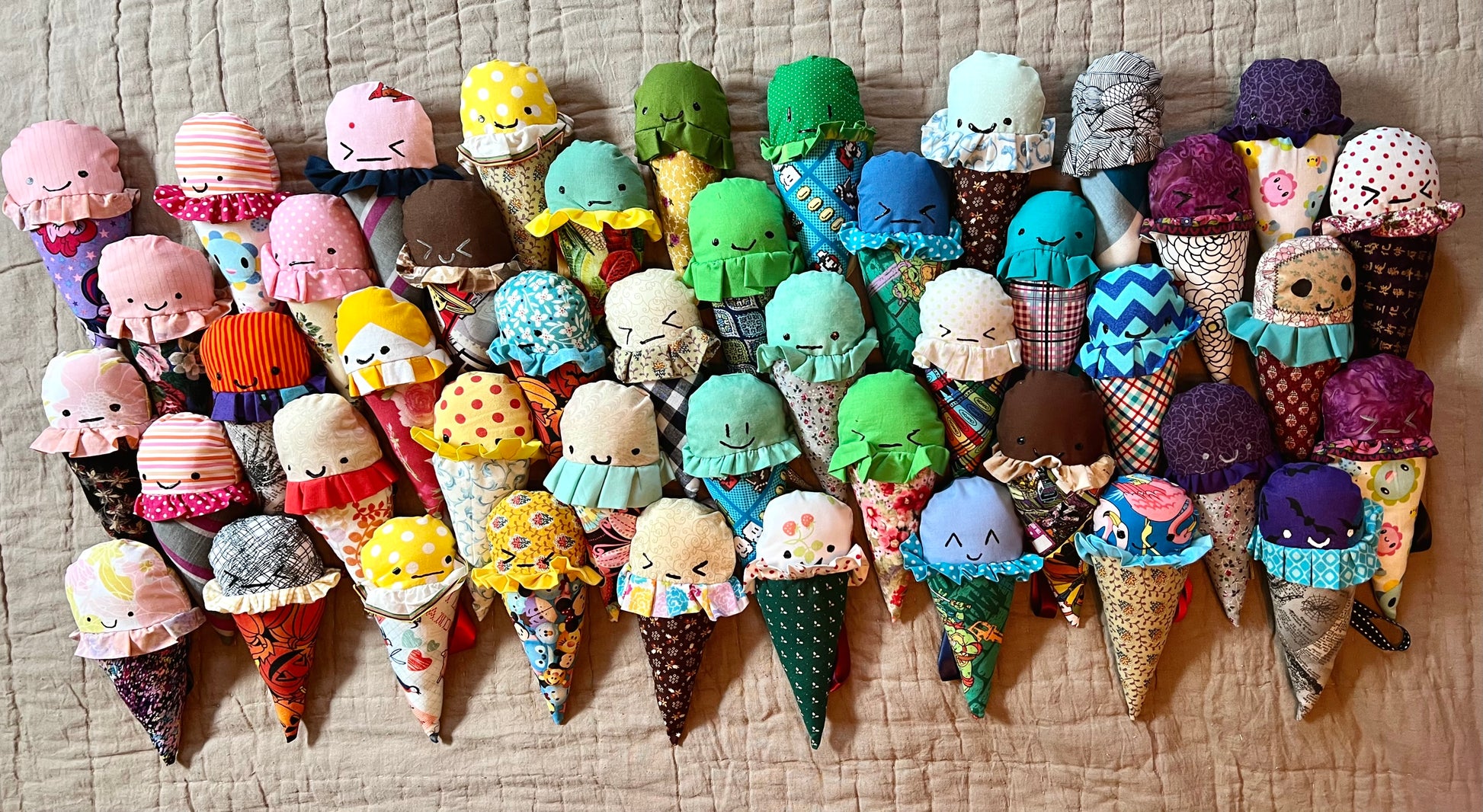 a rainbow of ice cream cone plushies, all lined up. some are smiling, some are grimacing, some are ambivalent, ALL ARE CUTE