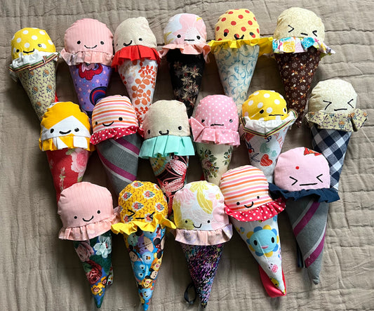A group of colorful ice cream cone plushies, all lined up next to each other. Aerial view against a quilted background.