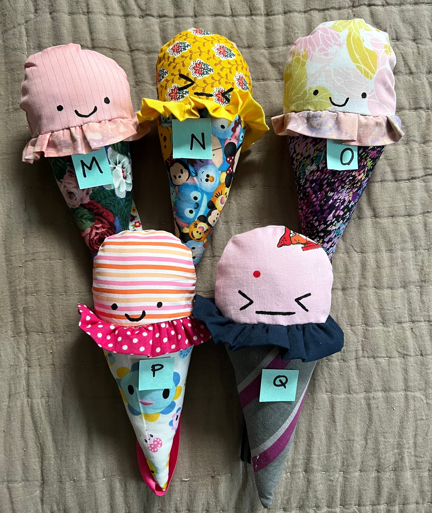 Ice cream cone plushies with handpainted faces, lined up with the letters M N O P Q below them