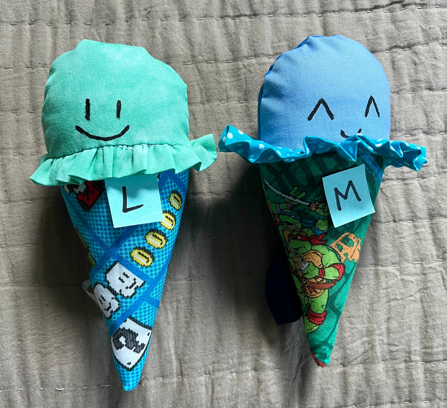 Ice cream cone plushies with handpainted faces, lined up with the letters L M below them