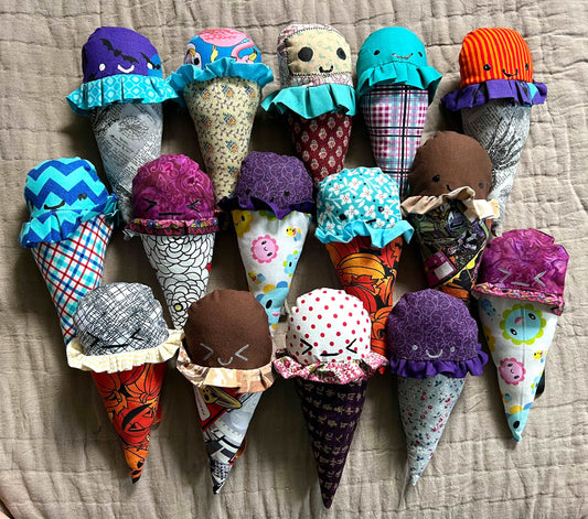 A group of colorful ice cream cone plushies, all lined up next to each other. Aerial view against a quilted background.
