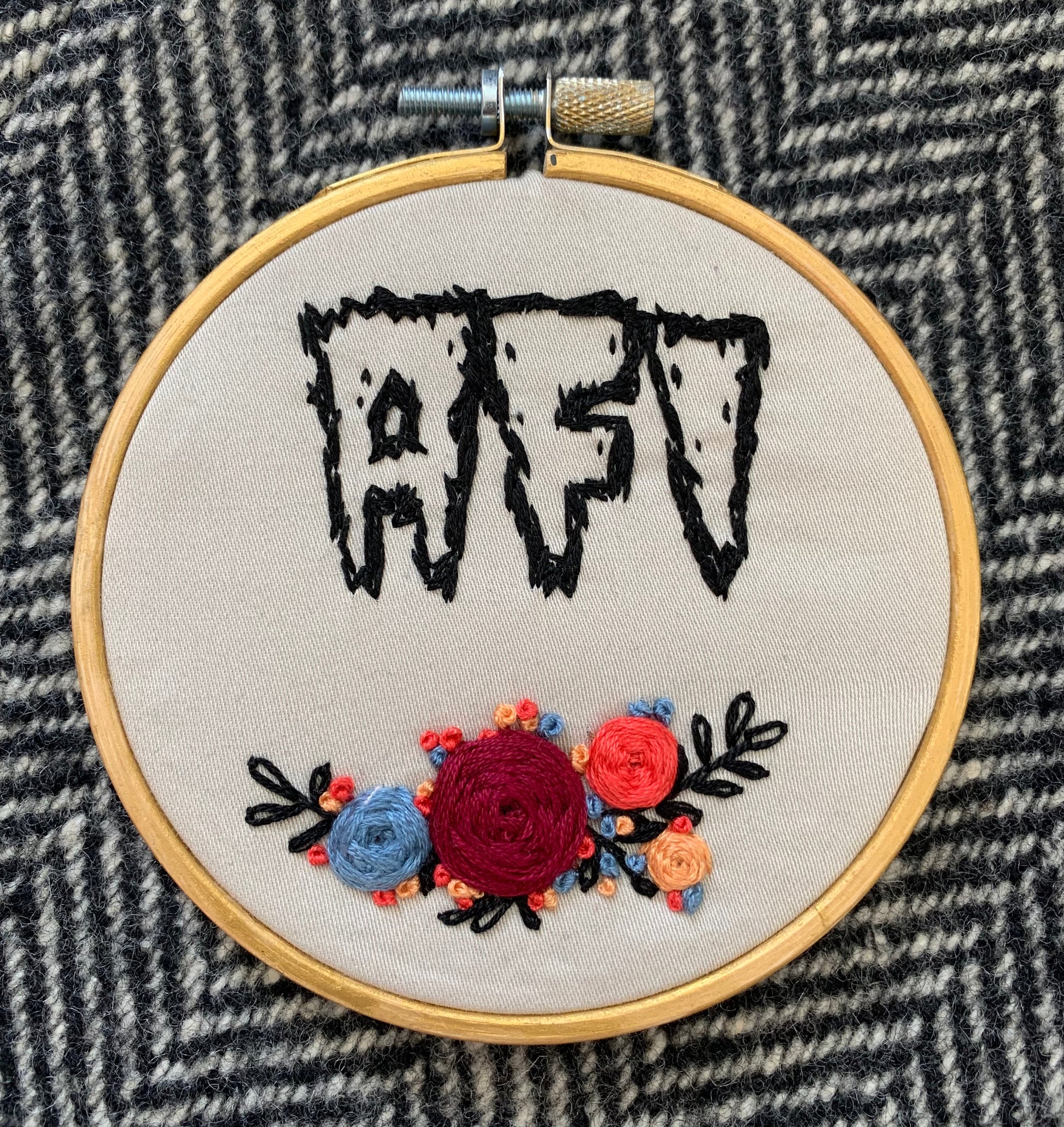 an embroidery hoop, painted gold, with florals and the letters "AFI"