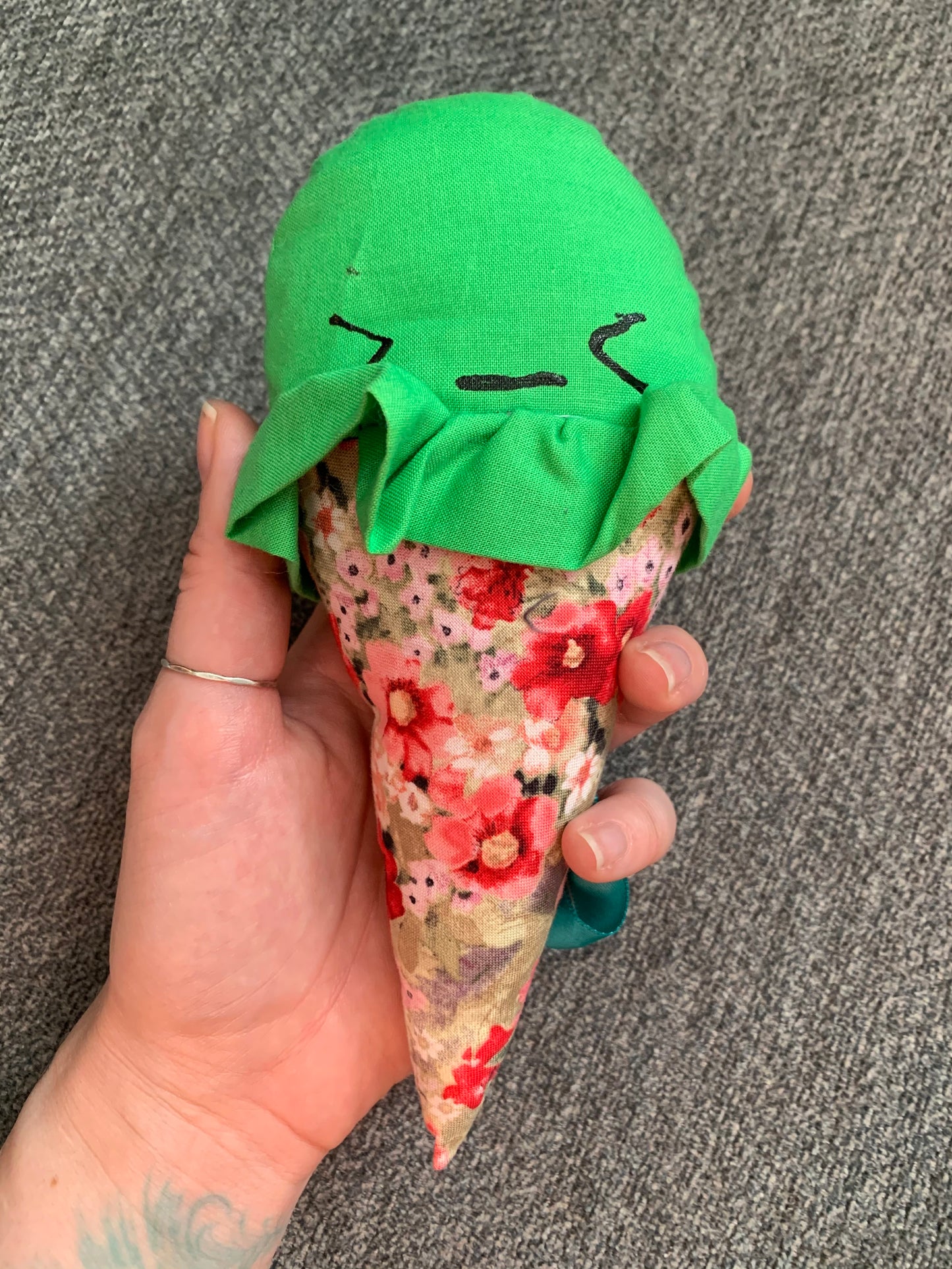 a green ice cream cone with pink and red floral cone, held up against a grey background, hand for scale