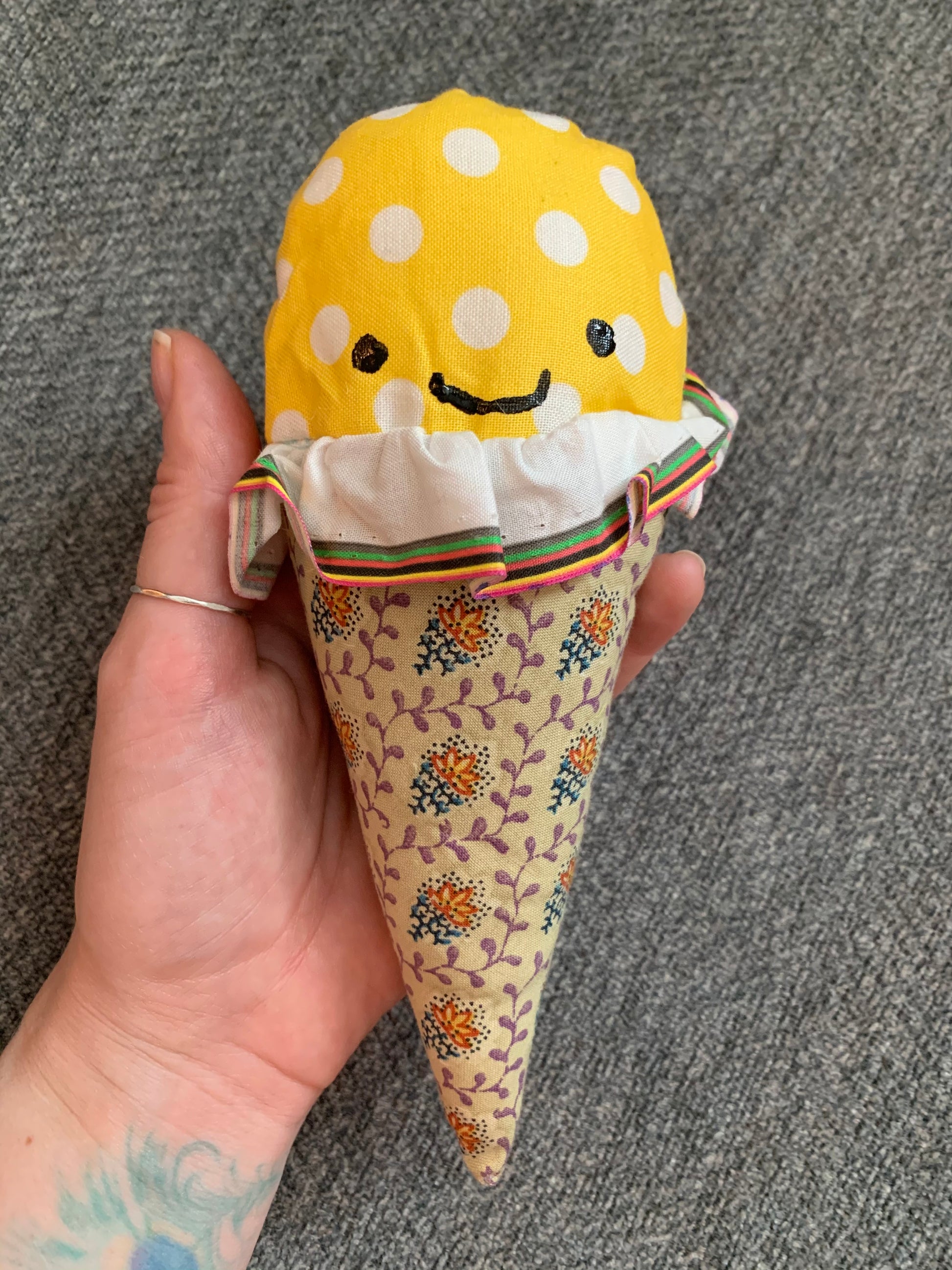 a yellow polkadot ice cream cone with khaki and yellow floral cone, held up against a grey background, hand for scale