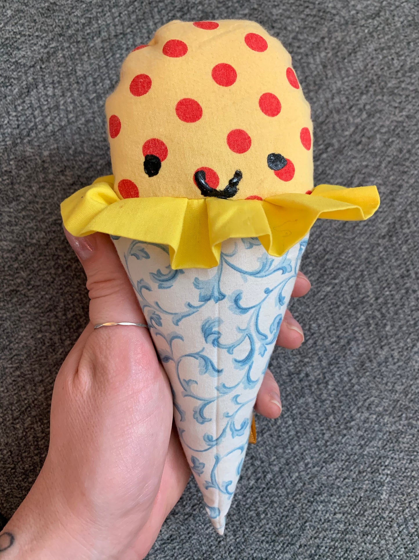 a yellow and red polkadot ice cream cone with light blue filigree cone, held up against a grey background, hand for scale