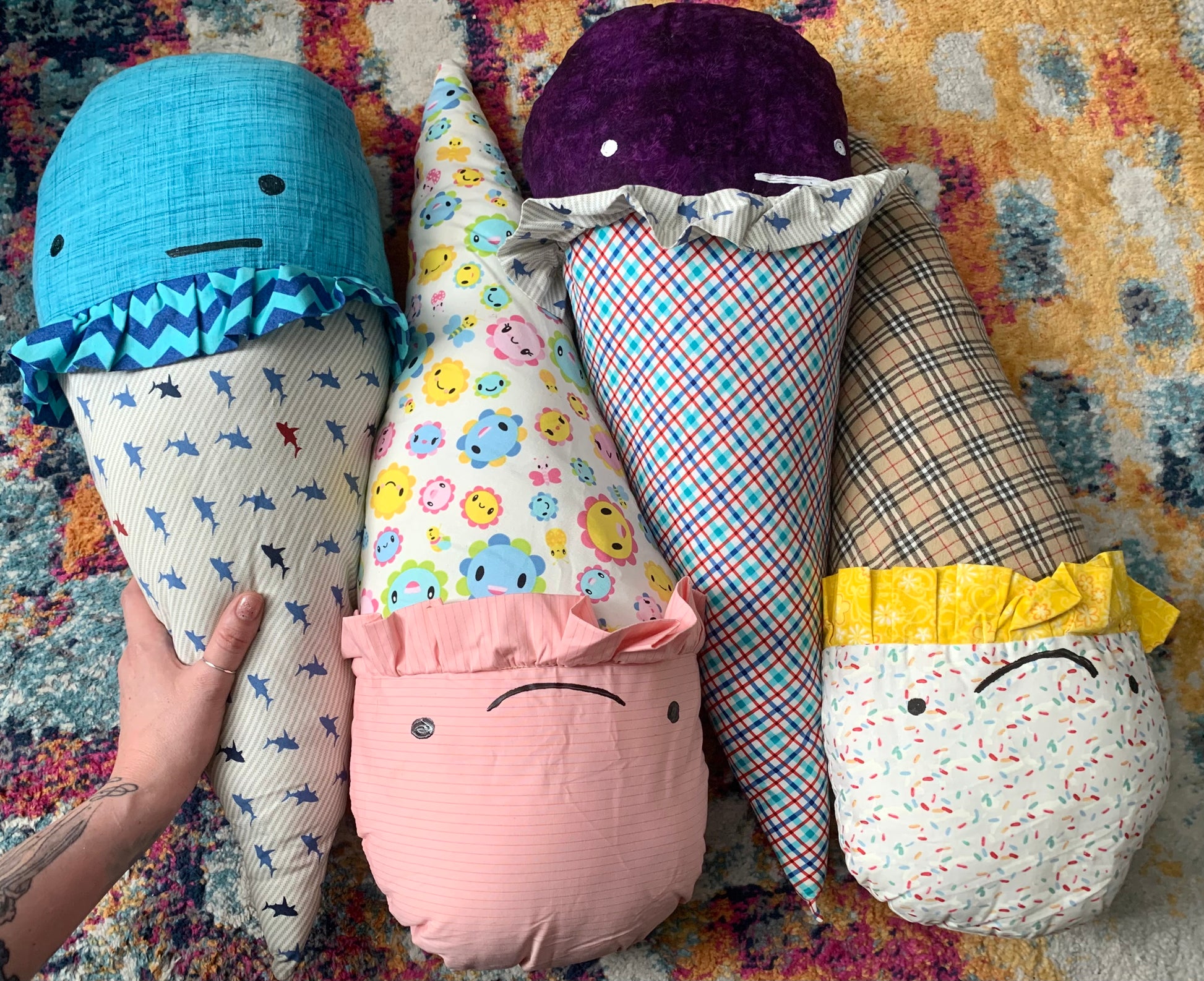 group shot, aerial view of GIANT ice cream cone pillows, with assorted faces, one hand holds the one on left, against a colorful background