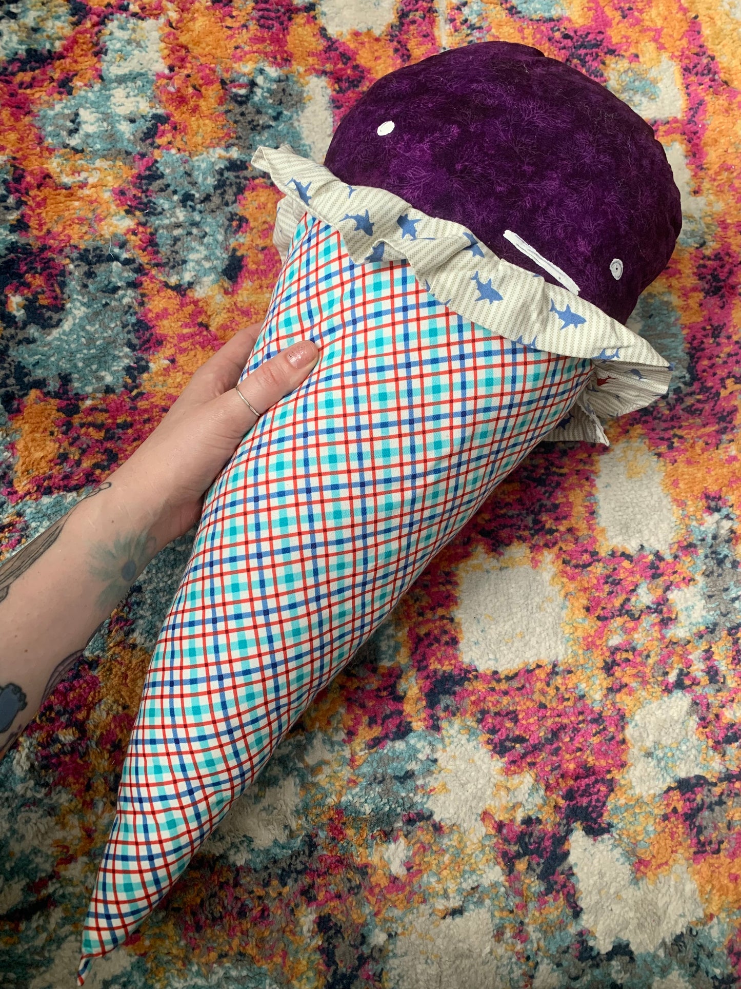 GIANT ice cream cone pillow, with Grape Sharkberry ice cream top, an indifferent white face, and a red and blue plaid cone. held by a hand for scale