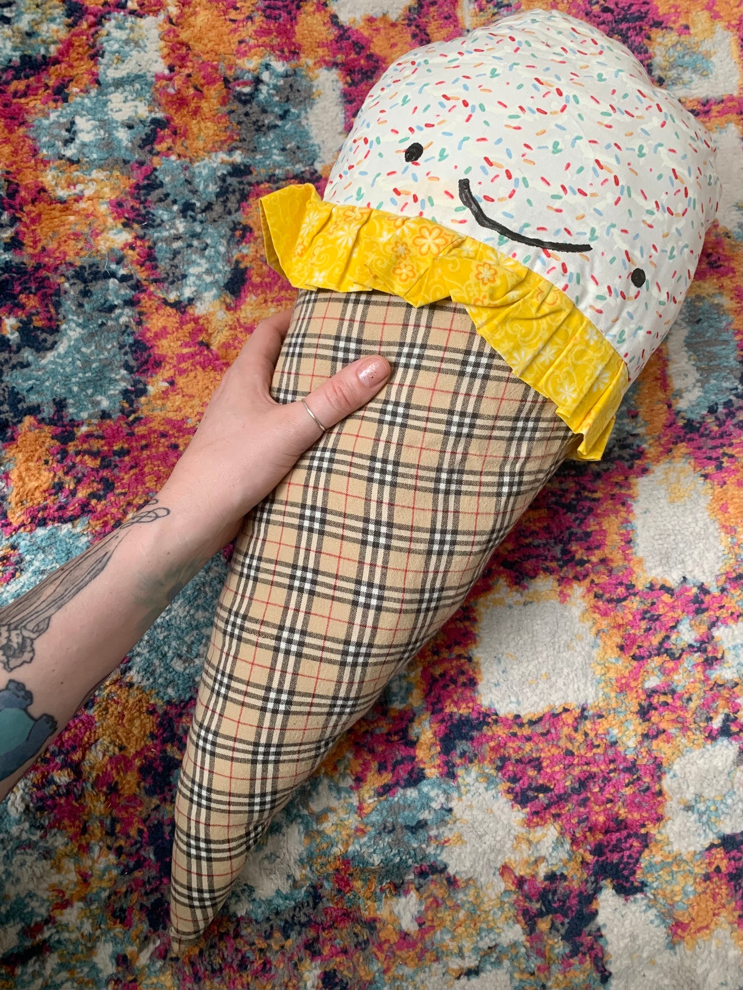 GIANT ice cream cone pillow, with white sprinkle and yellow floral fabric ice cream top, a happy face, and burberry plaid cone. held by a hand for scale