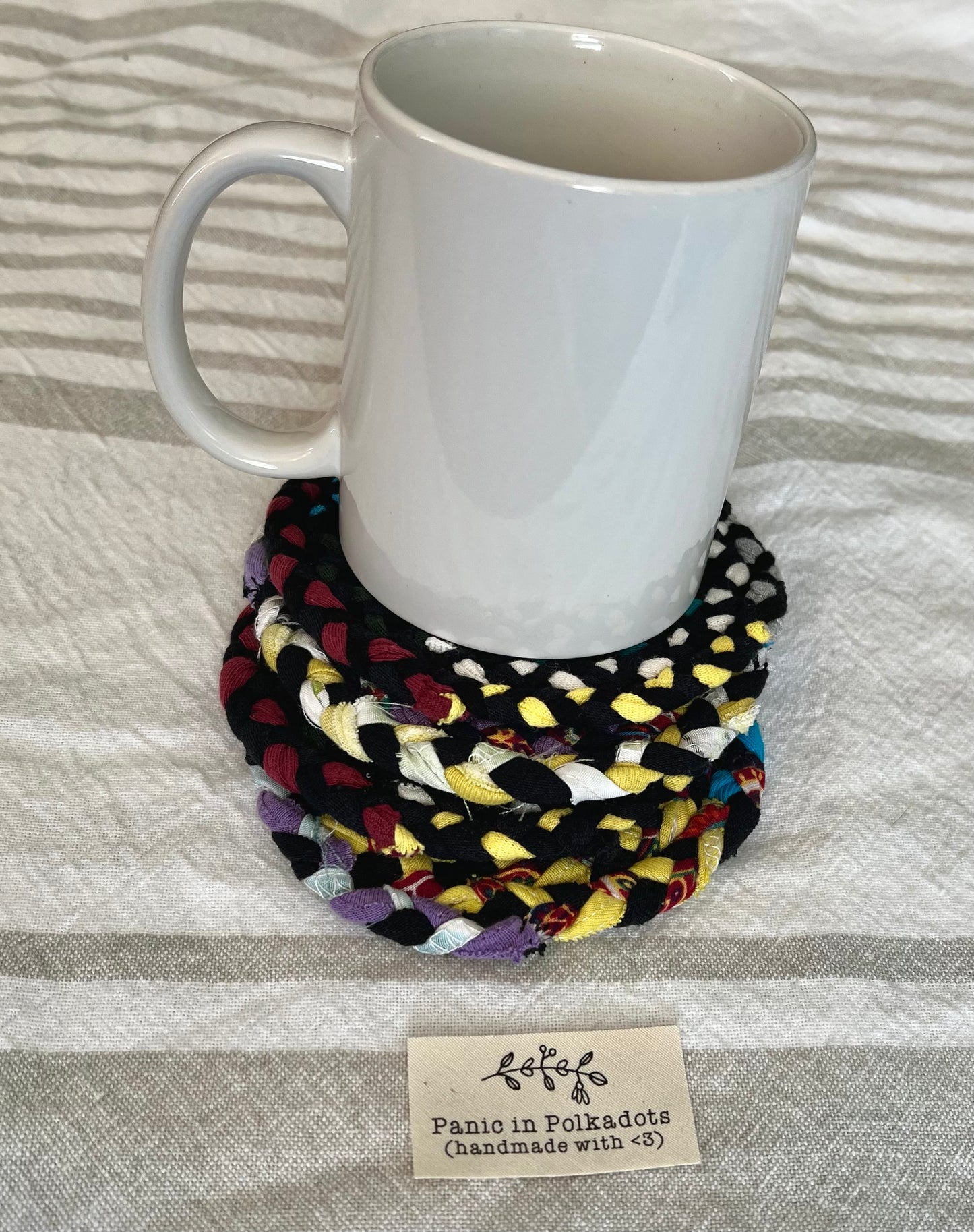 Mini rug coaster set, in a stack, with a white coffee mug on top, for scale and usage idea.