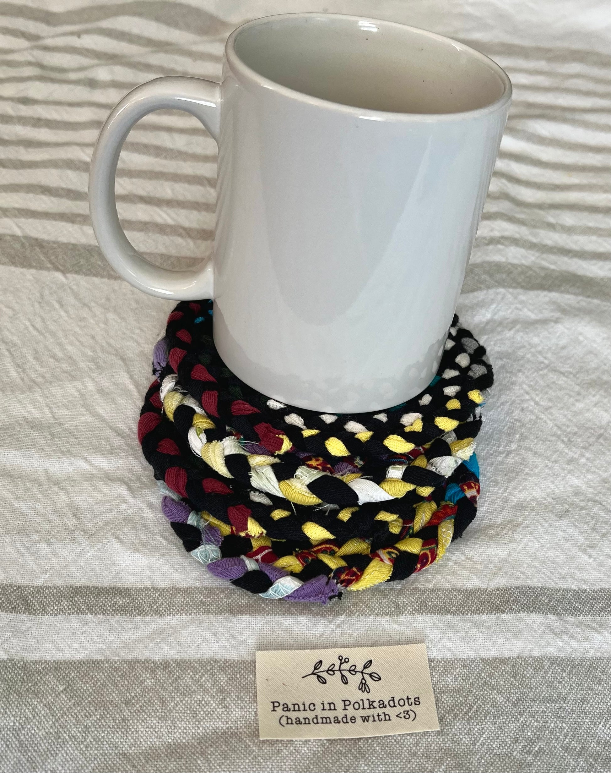 Mini rug coaster set, in a stack, with a white coffee mug on top, for scale and usage idea.