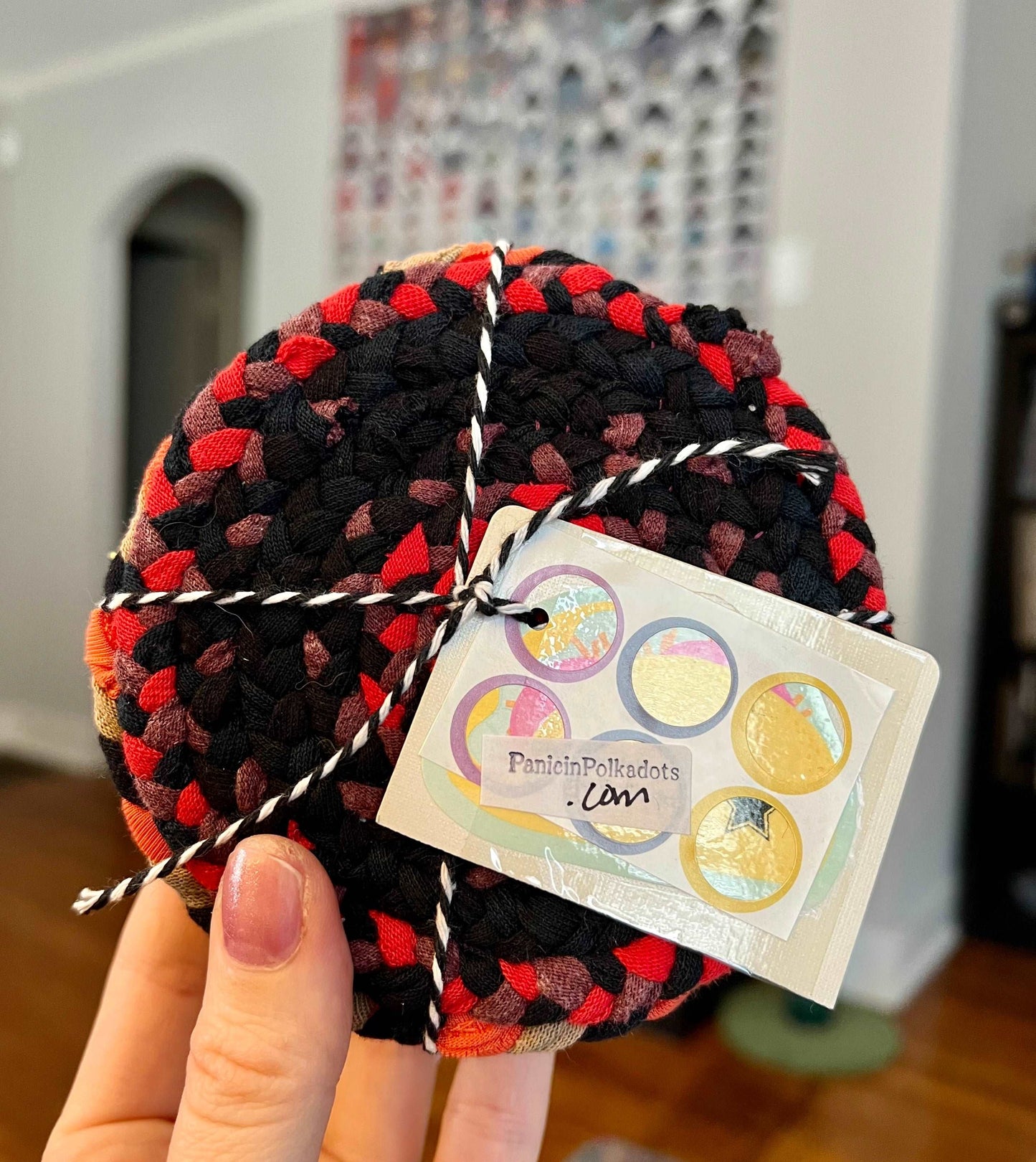 Mini rug coaster set, bound by string and a tag, held up by a hand, with a quilt in the background