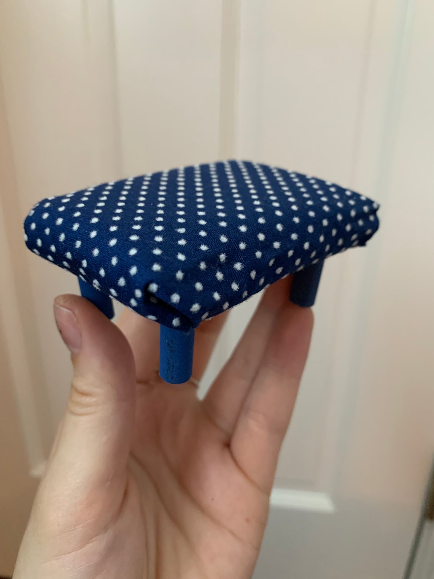 a miniature dollhouse ottoman, held in a hand for scale. This one is navy with white polkadots, with navy legs