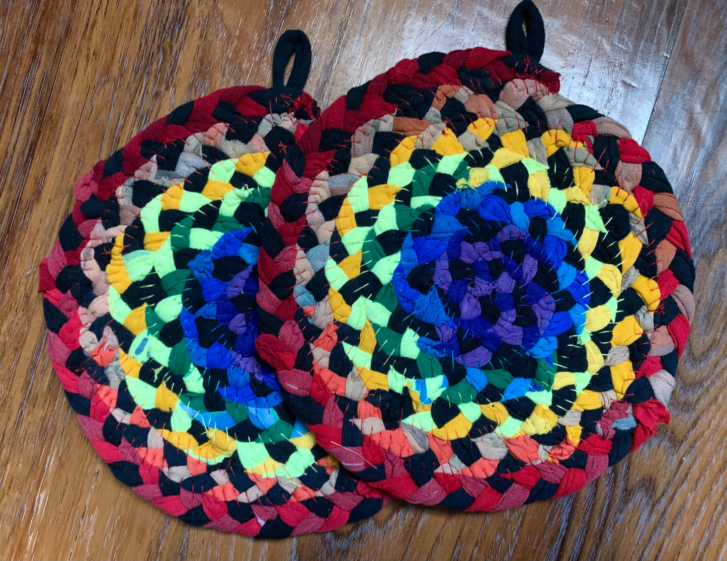 The back of two trivet potholders, to show off stitching, lay flat on a wood surface.