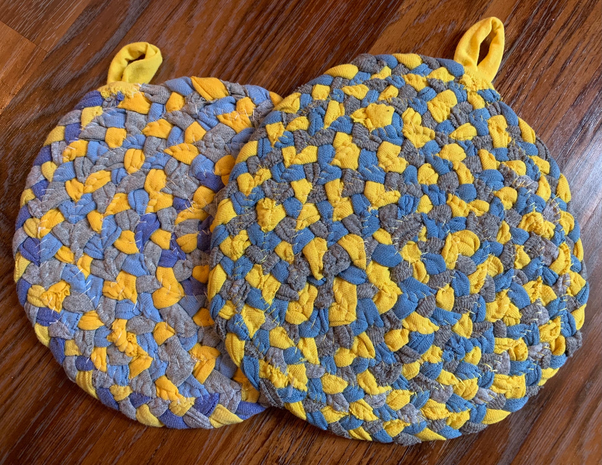 The back of two trivet potholders, to show off stitching, lay flat on a wood surface.