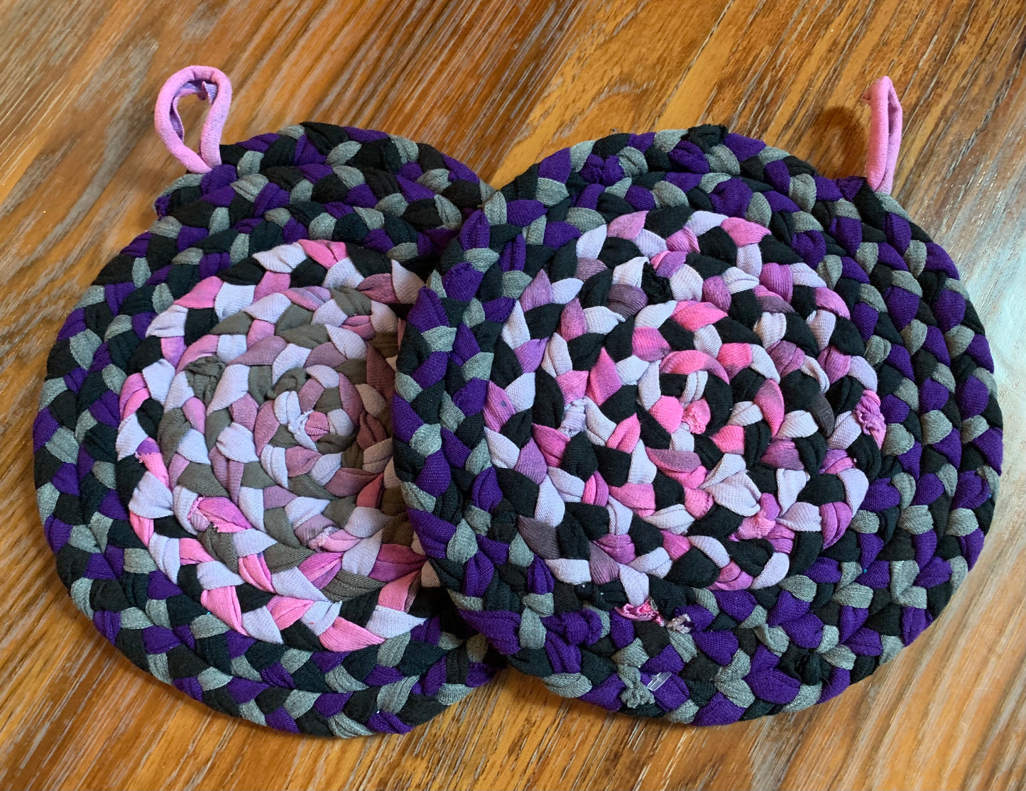 A set of two trivet potholders, side by side, lay flat on a wood surface.