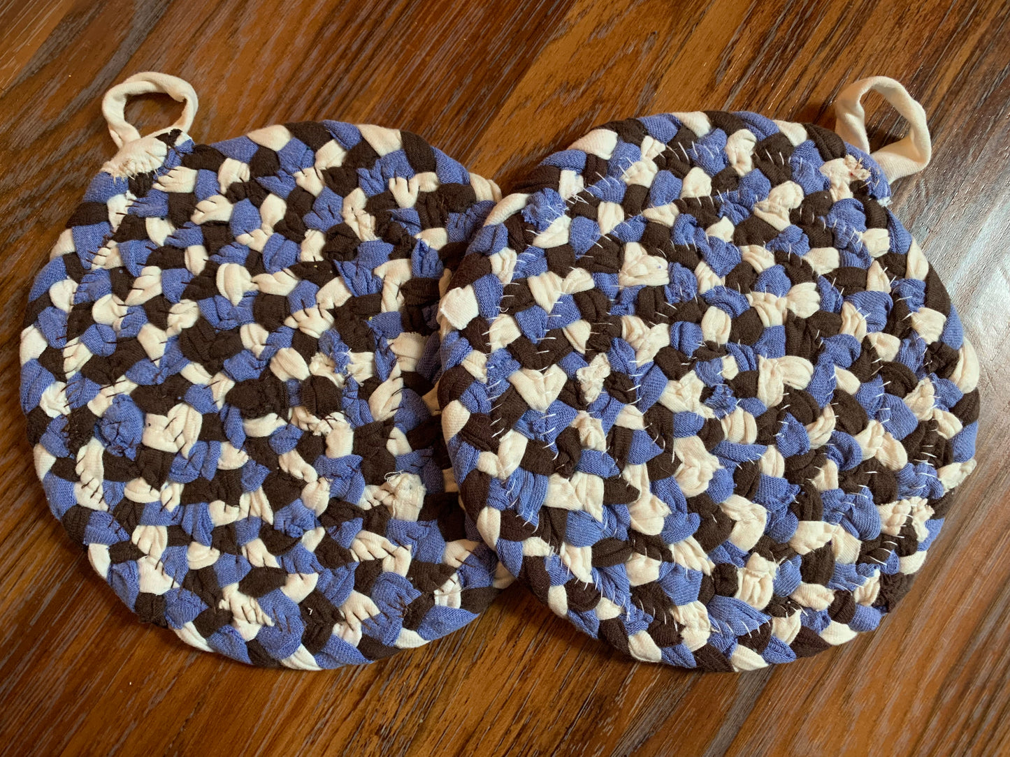 The back of two trivet potholders, to show off stitching, lay flat on a wood surface.