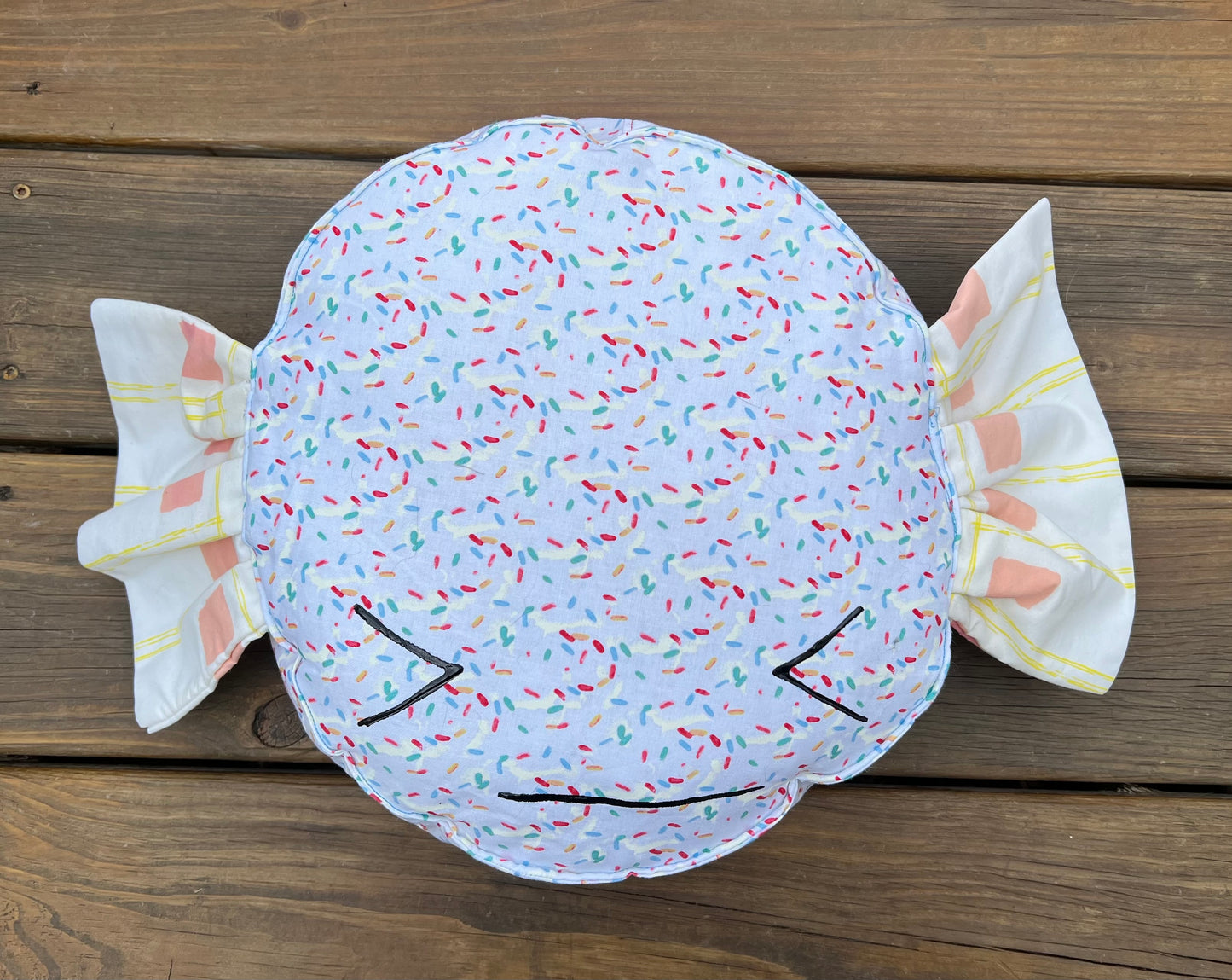 Sprinkle Delight candy pillow, against a wood background, with a painted face.