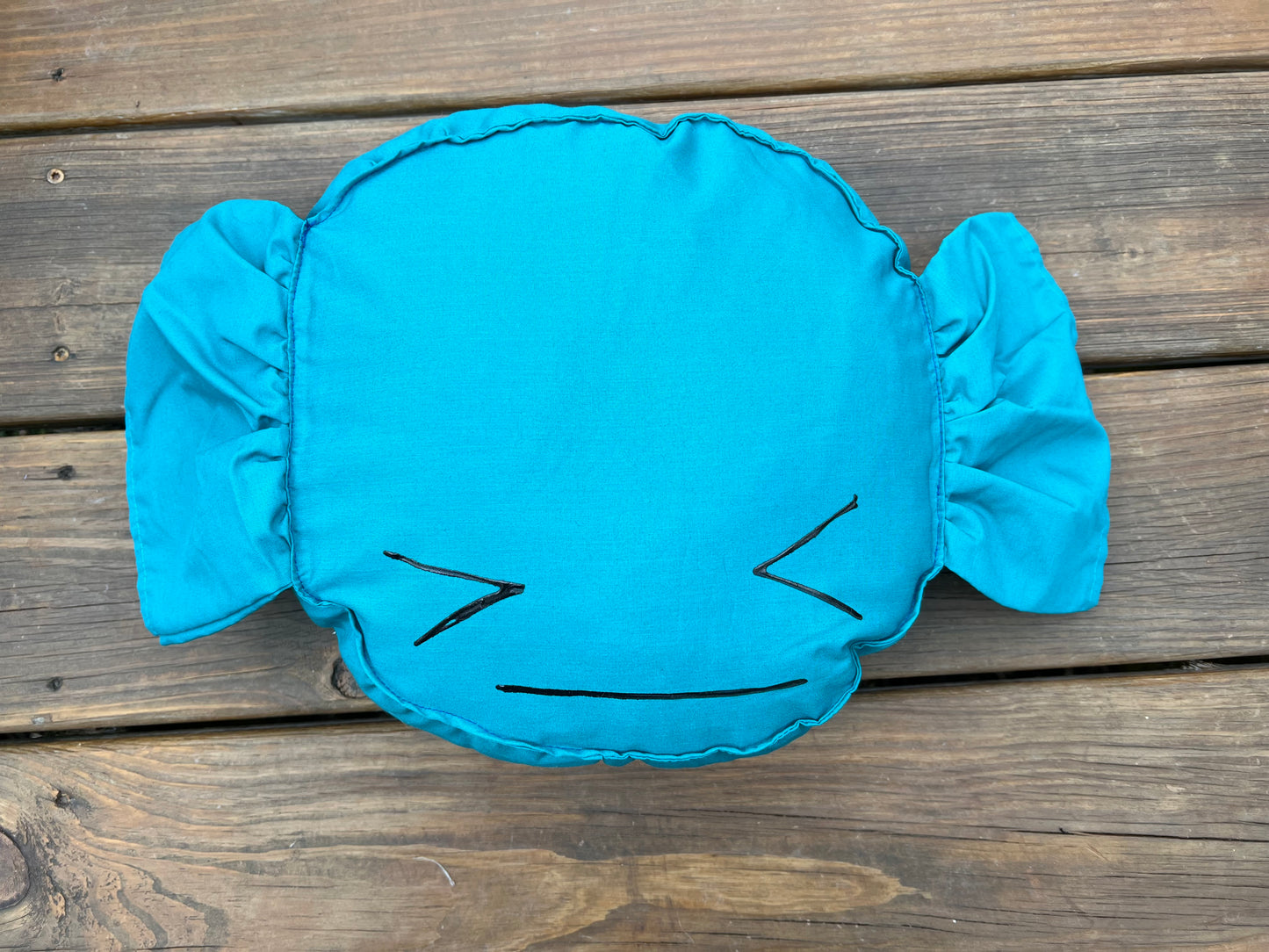 Blue Raspberry candy pillow, against a wood background, with a painted face.