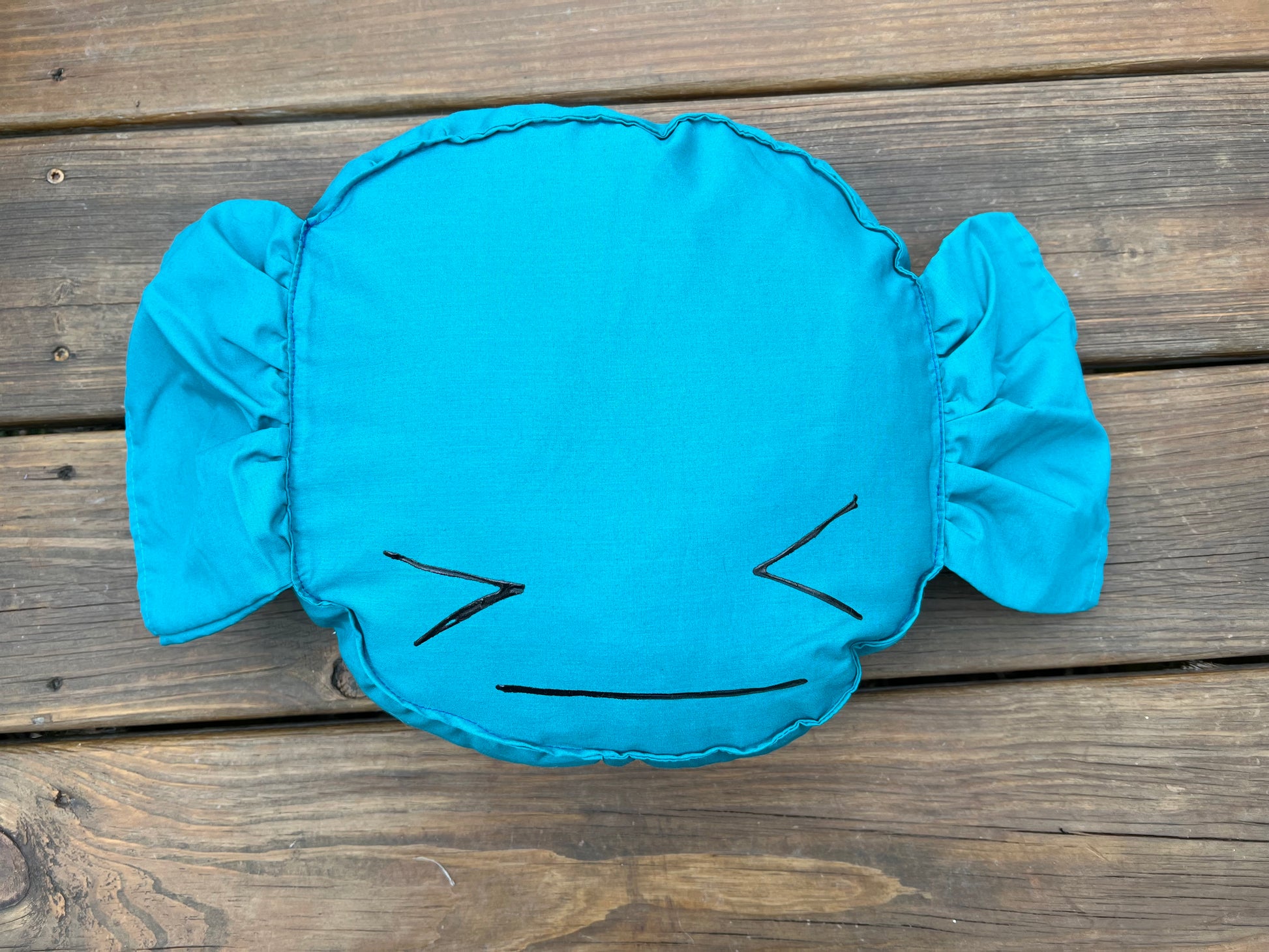 Blue Raspberry candy pillow, against a wood background, with a painted face.