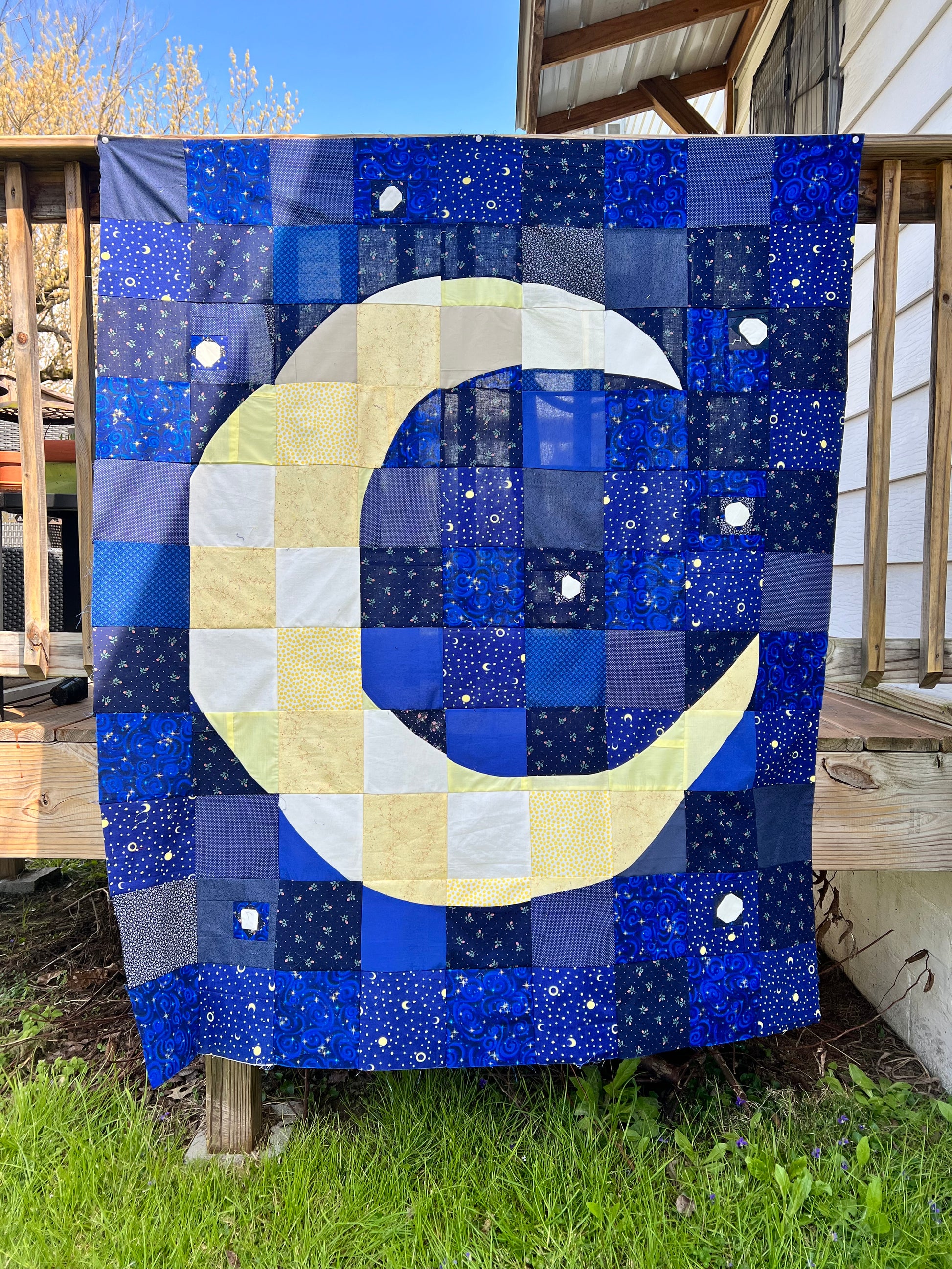 the quilt top only, prior to quilt sandwich and quilting. it hangs along a porch railing outside, with sun shining on it