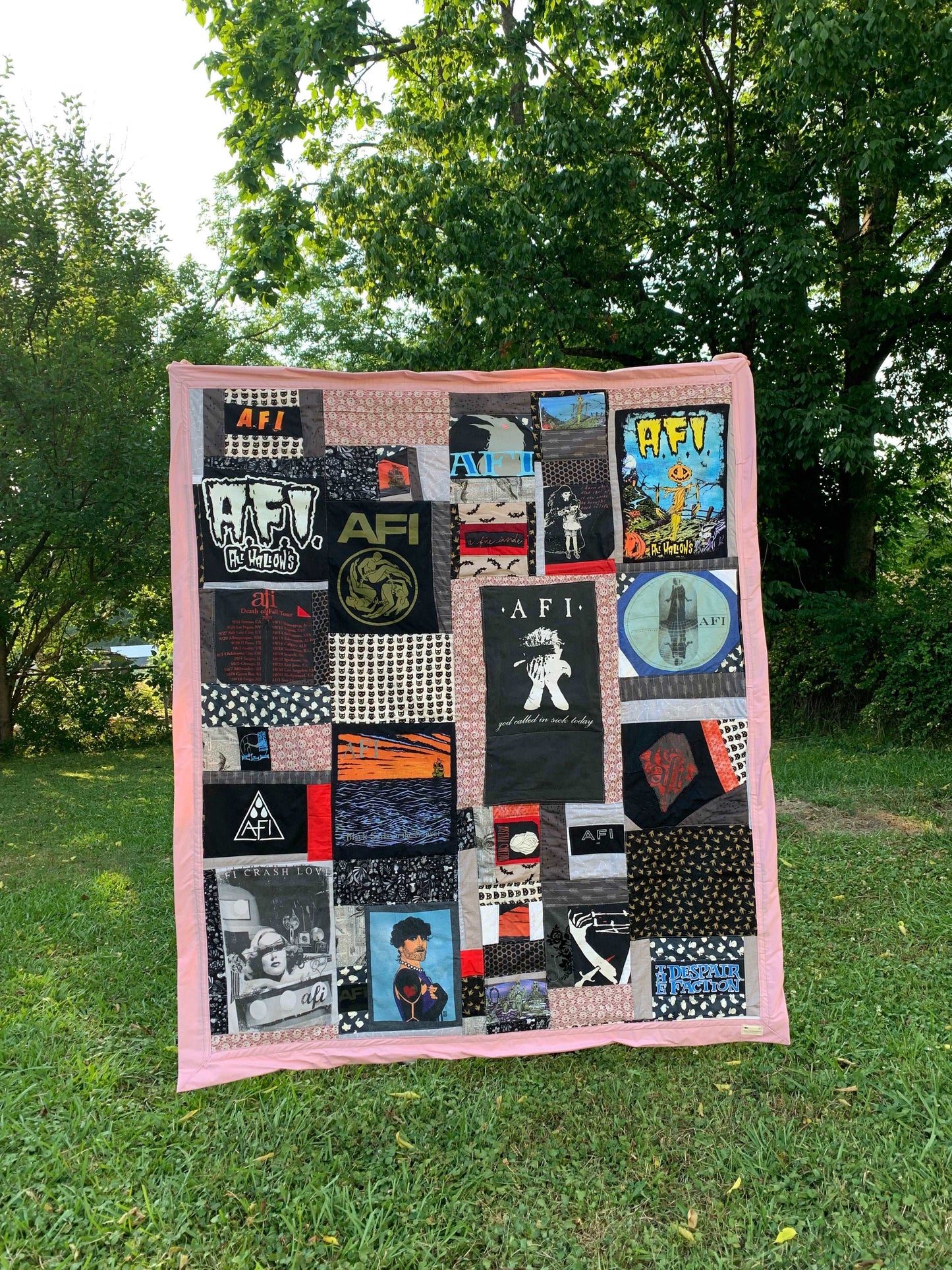 A tshirt quilt, featuring the band AFI (A Fire Inside) is held up outside with a green background and lawn.