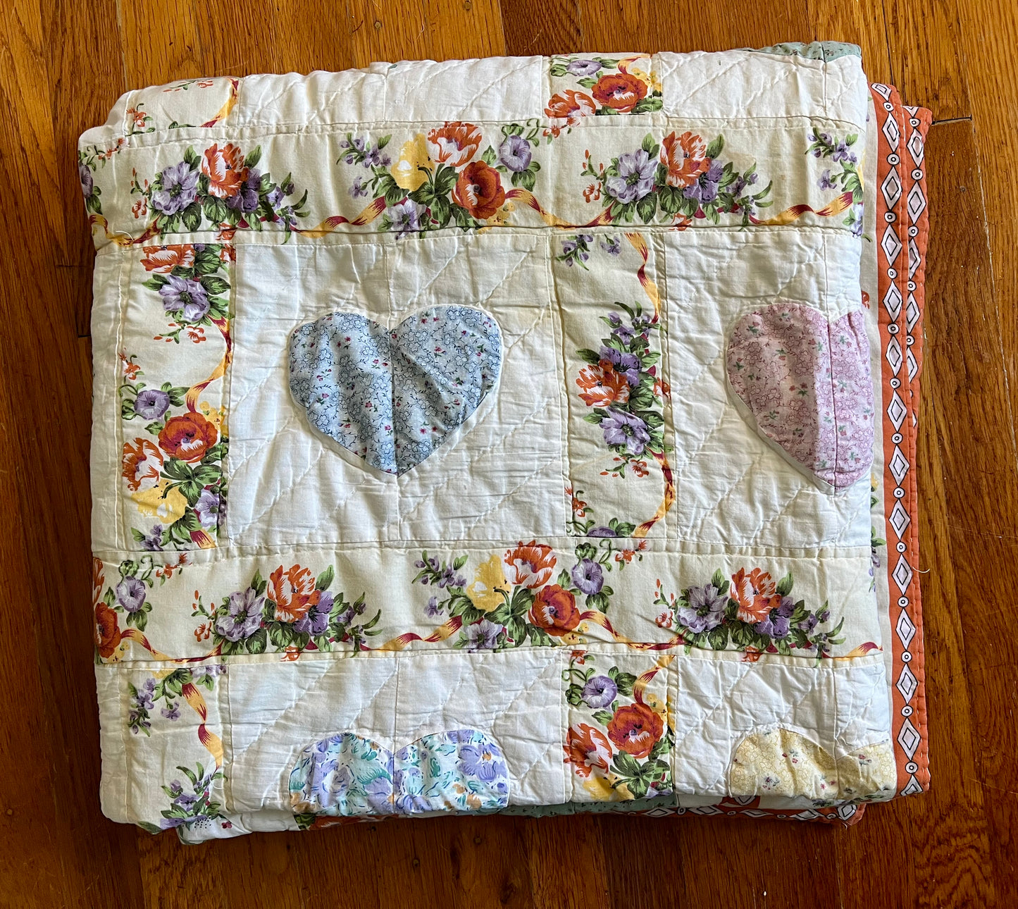 the quilt is folded neatly, and lays on top of a wood floor
